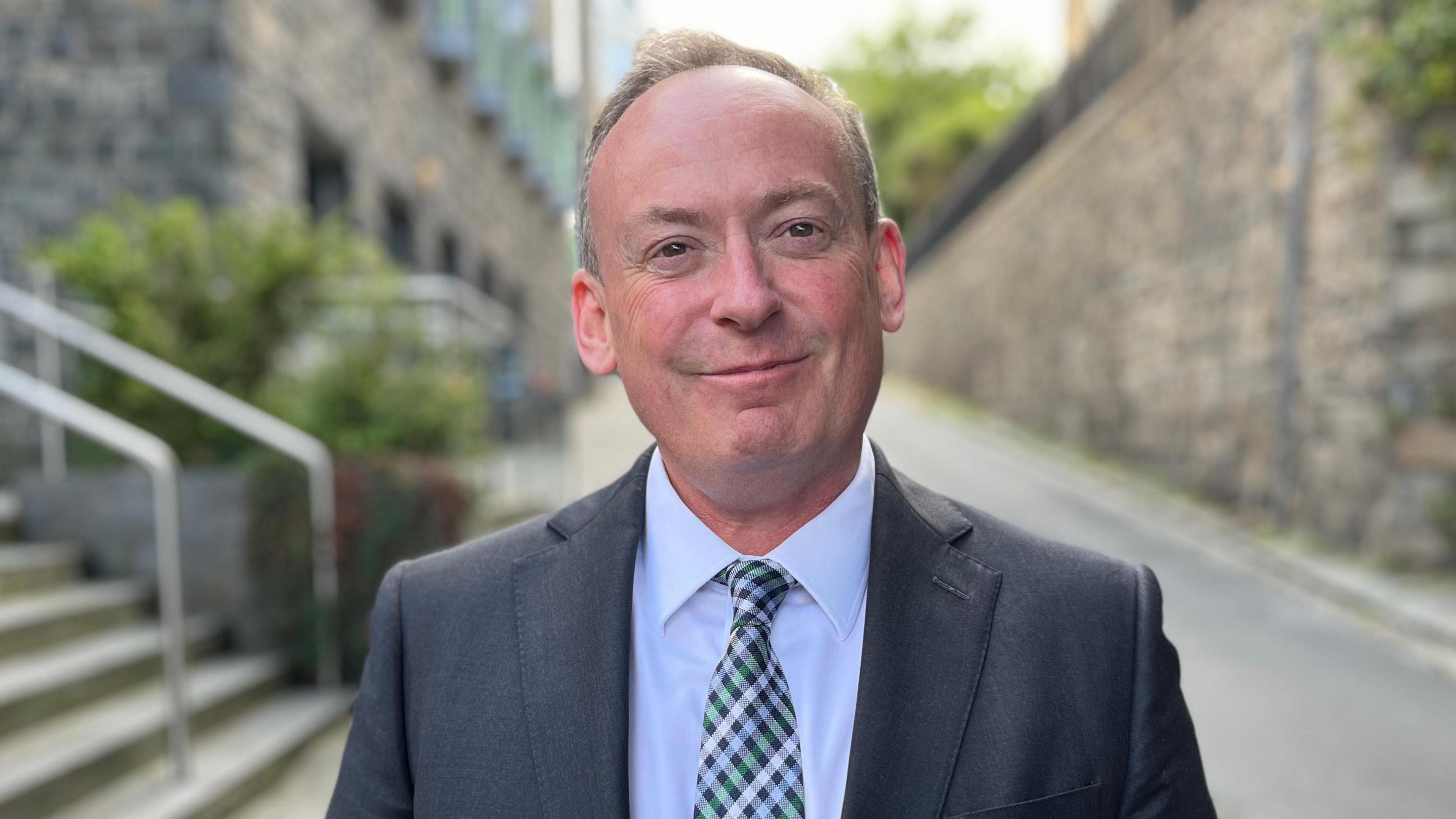 Deputy Lyndon Trott smiling wearing a suit and a checkered tie. 