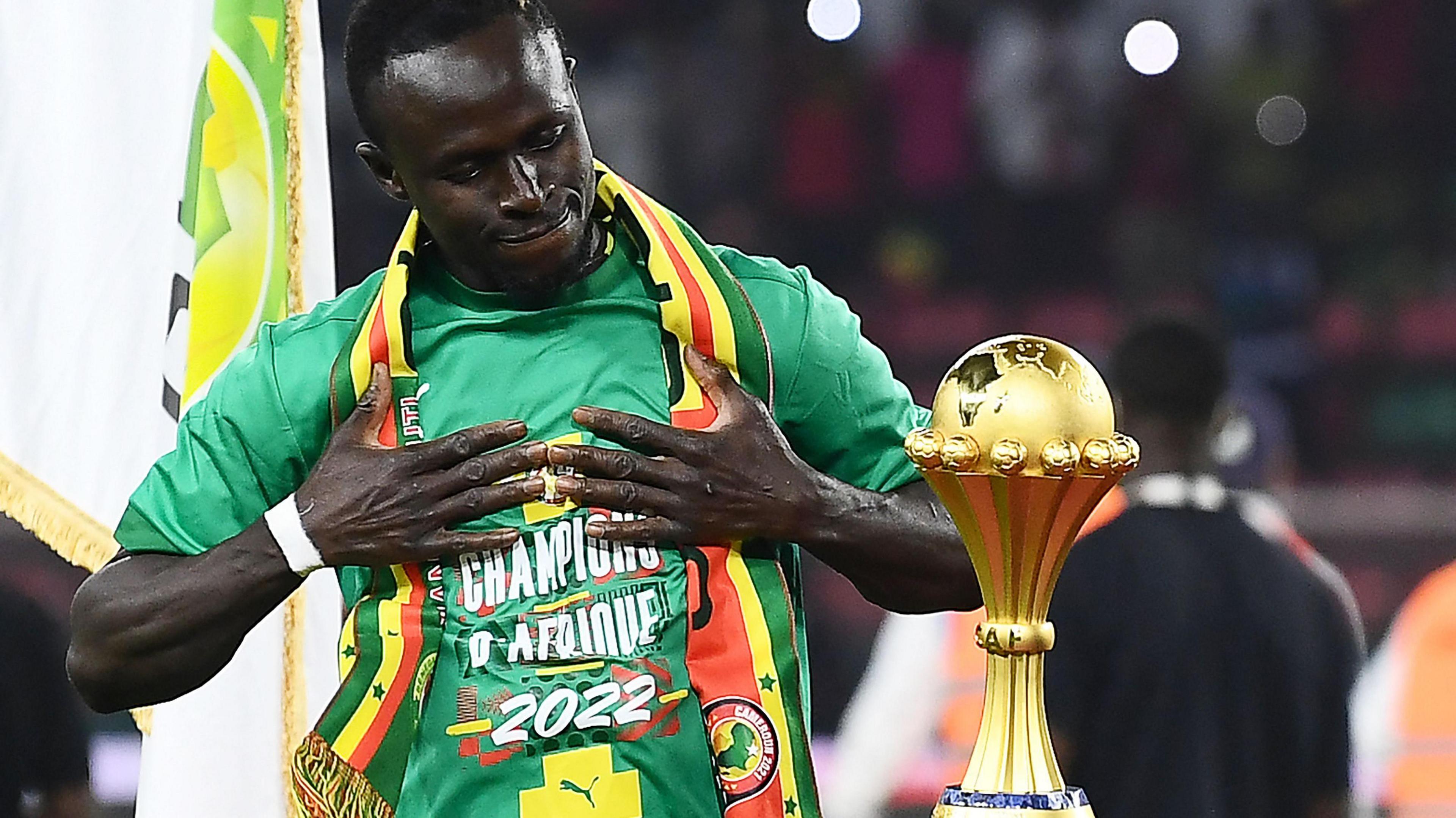 Sadio Mane holds his hands to his chest as he admires the Africa Cup of Nations trophy, which stands on a plinth