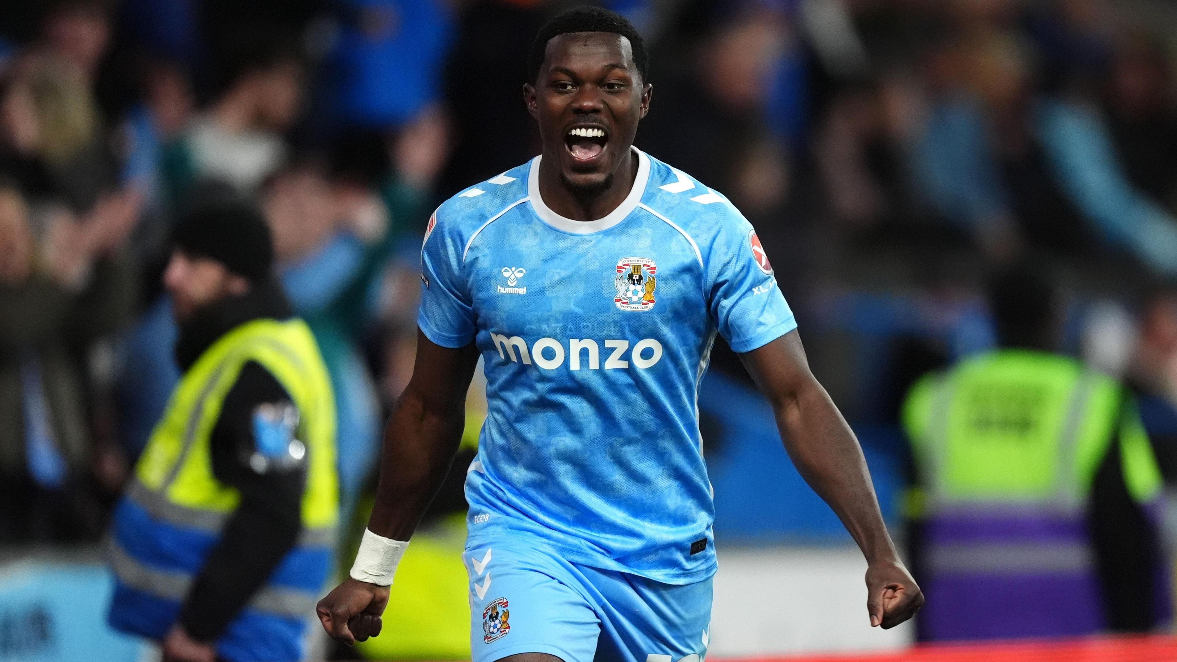 Ephron Mason-Clark, wearing Coventry City's sky blue home kit, celebrates a goal in the 5-1 win over Portsmouth, with his arms down by his sides and fists clenched, while his mouth is wide open as he shouts with happiness