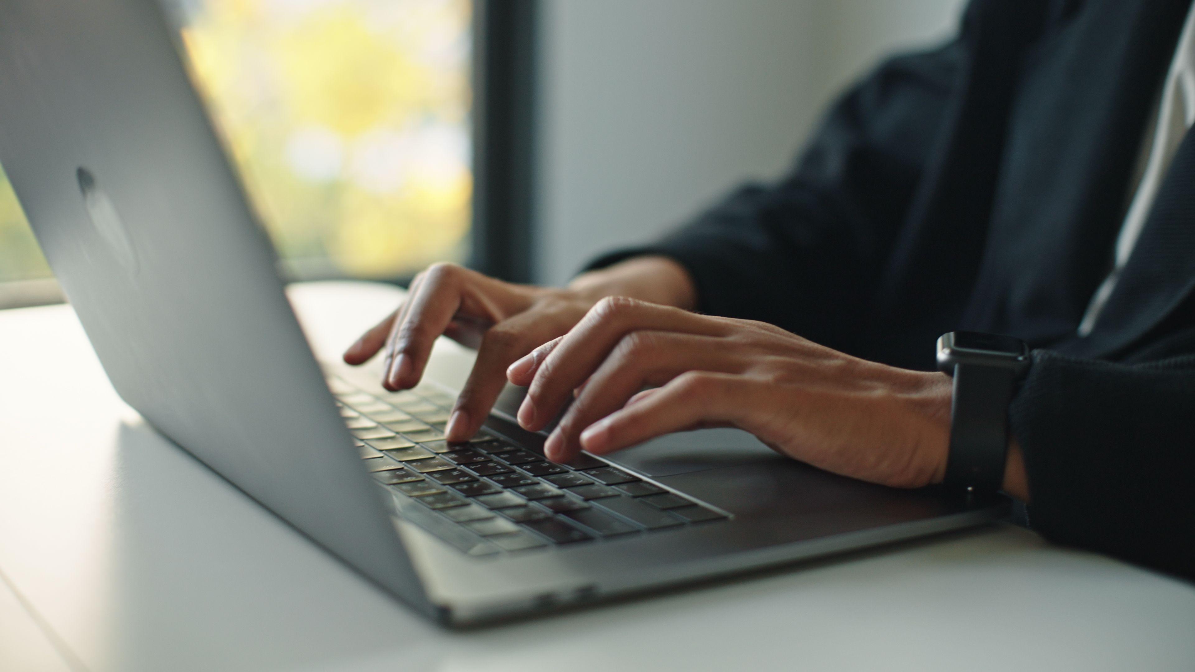 A man's hands seen typing on a laptop keyboard