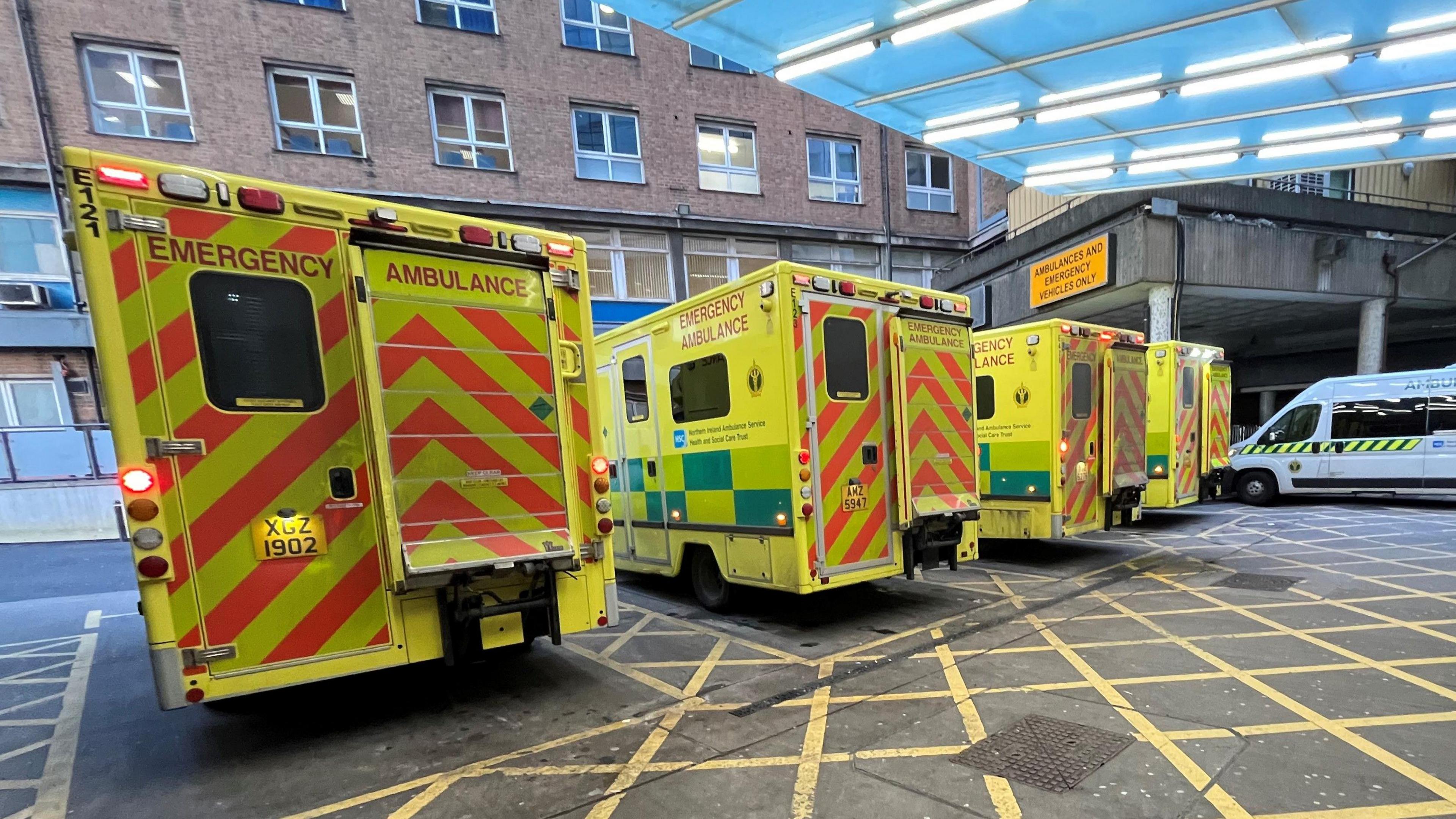 The outside of an Emergency Department main entrance. 5 ambulances are parked outside.