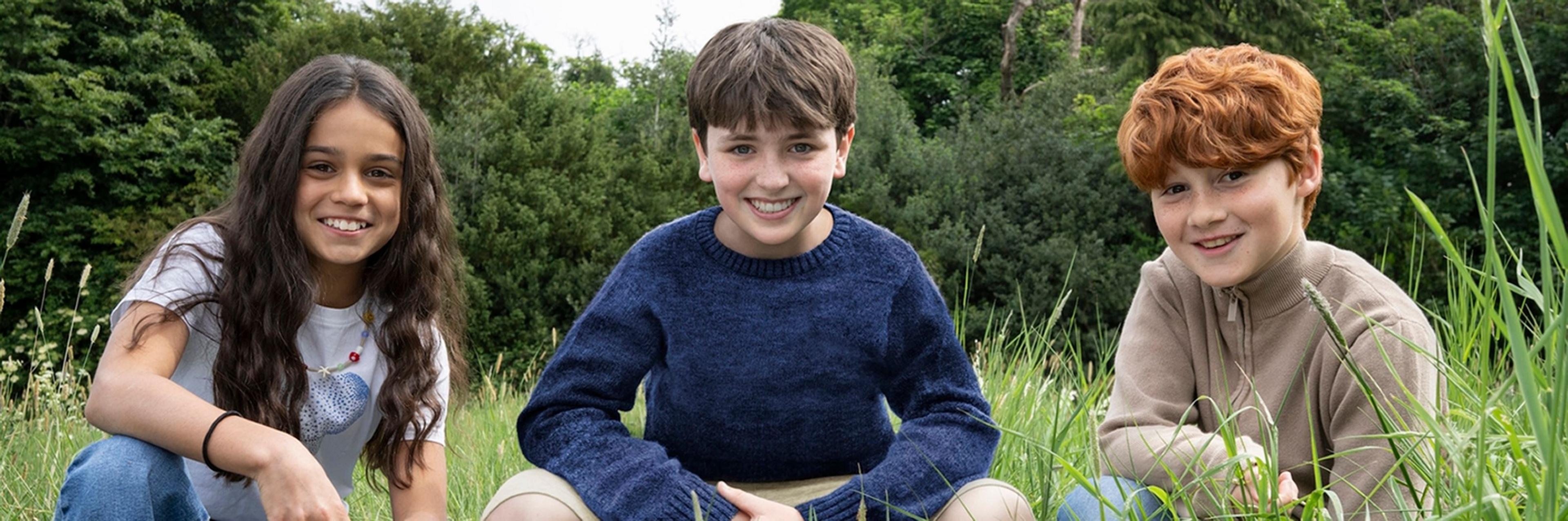Arabella Stanton, Dominic McLaughlin and Alastair Stout smiling while crouching in a field