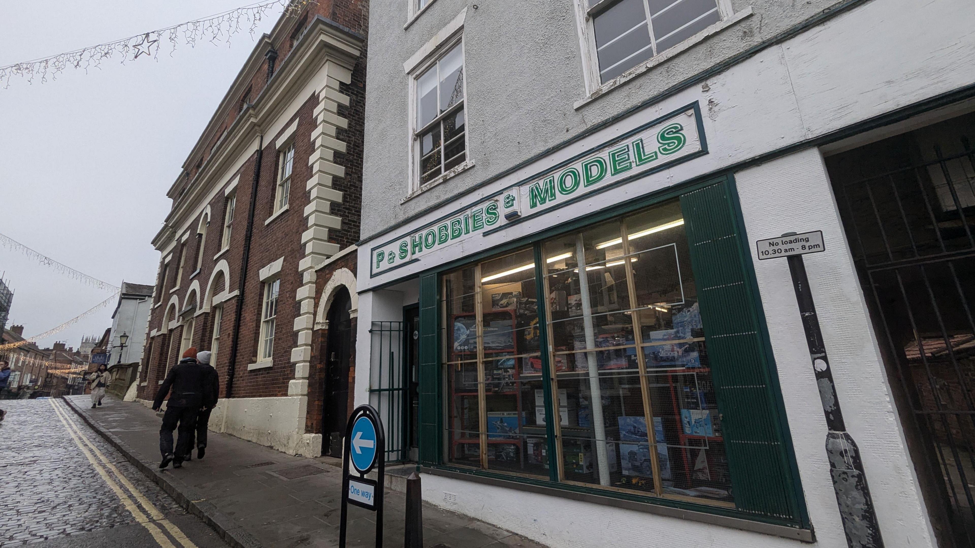 The shop front of P&S Hobbies and Models with a which background and green lettering, and model kits in the window. 