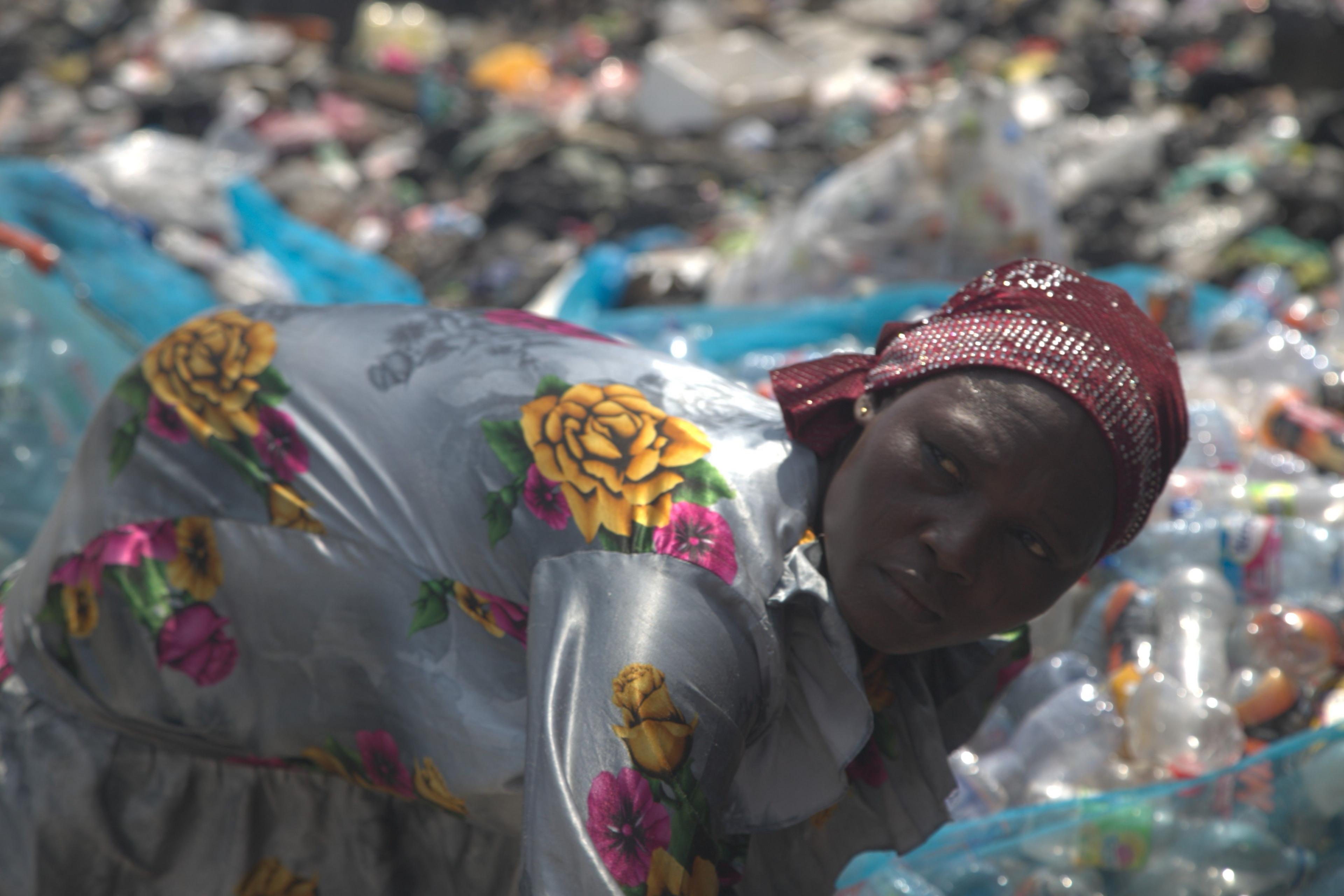 Abiba Alhassan, a woman wearing a floral dress and a headscarf, sorts out used plastic bottles next to the Agbogbloshie dumpsite in Accra