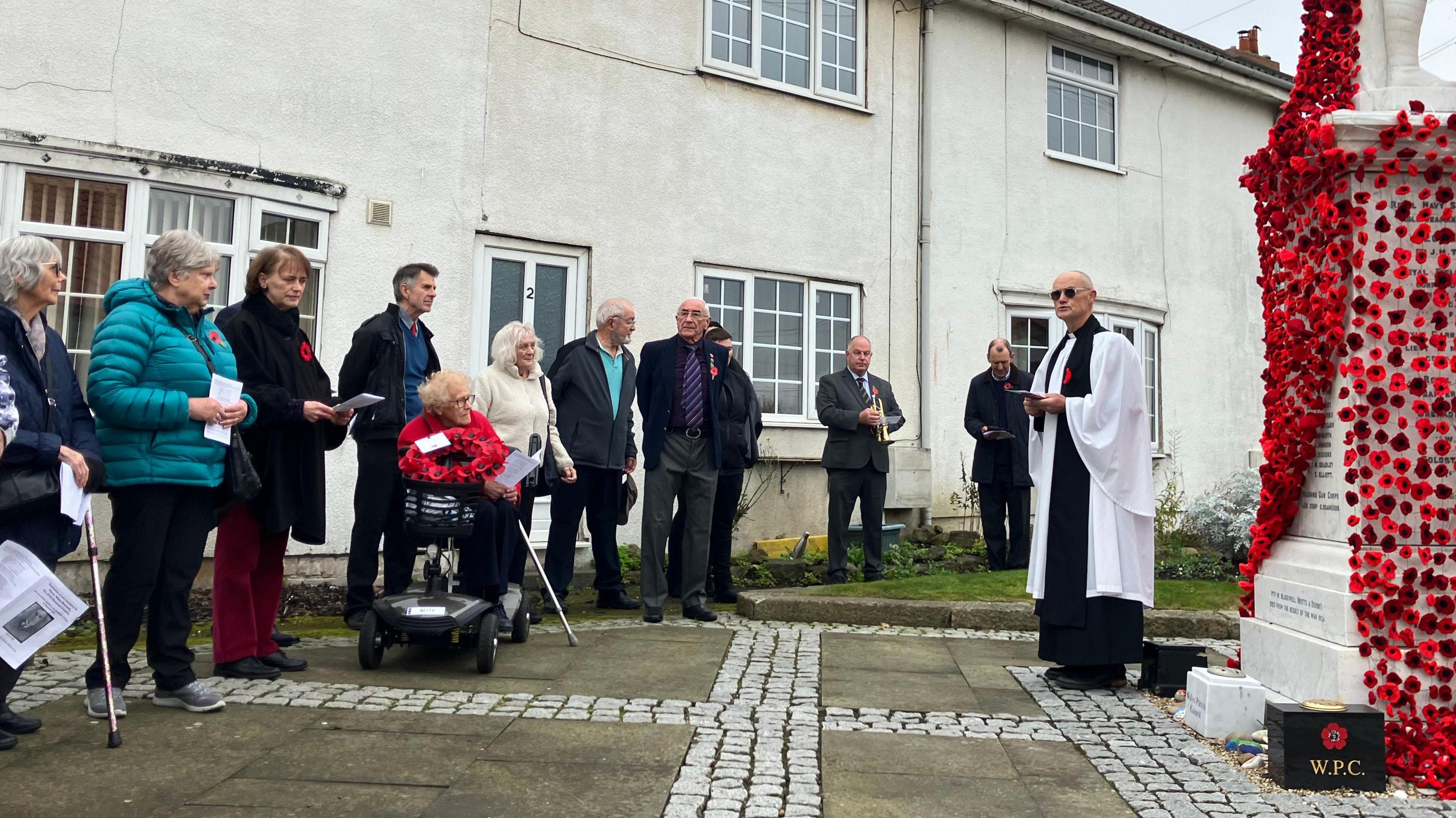 A priest and several people are gathered around the cenotaph for the service - including Betty, who's on a mobility scooter.