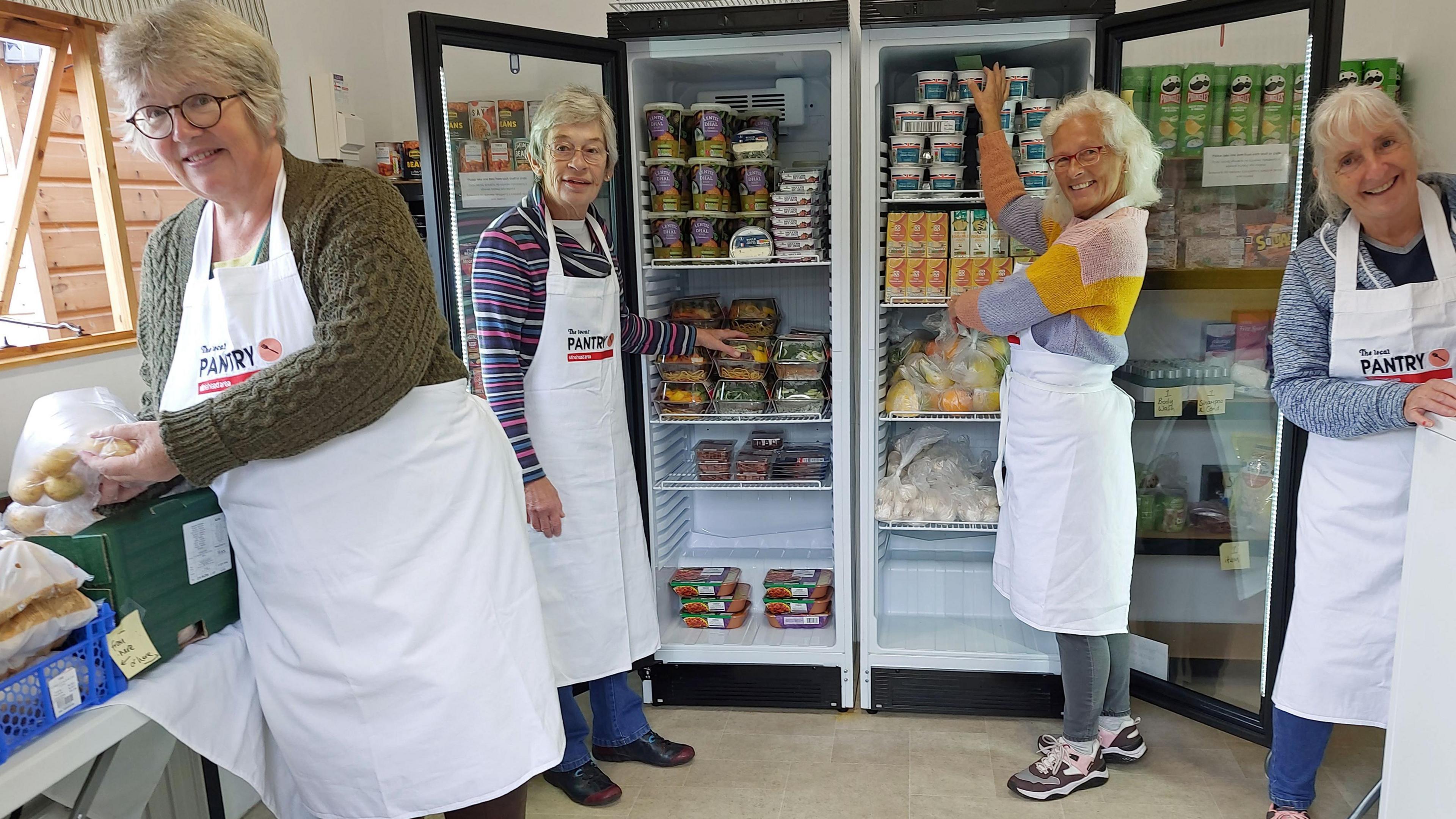 Volunteers from the West Somerset Food Cupboard are stood in front of a fridge fully stocked with produce