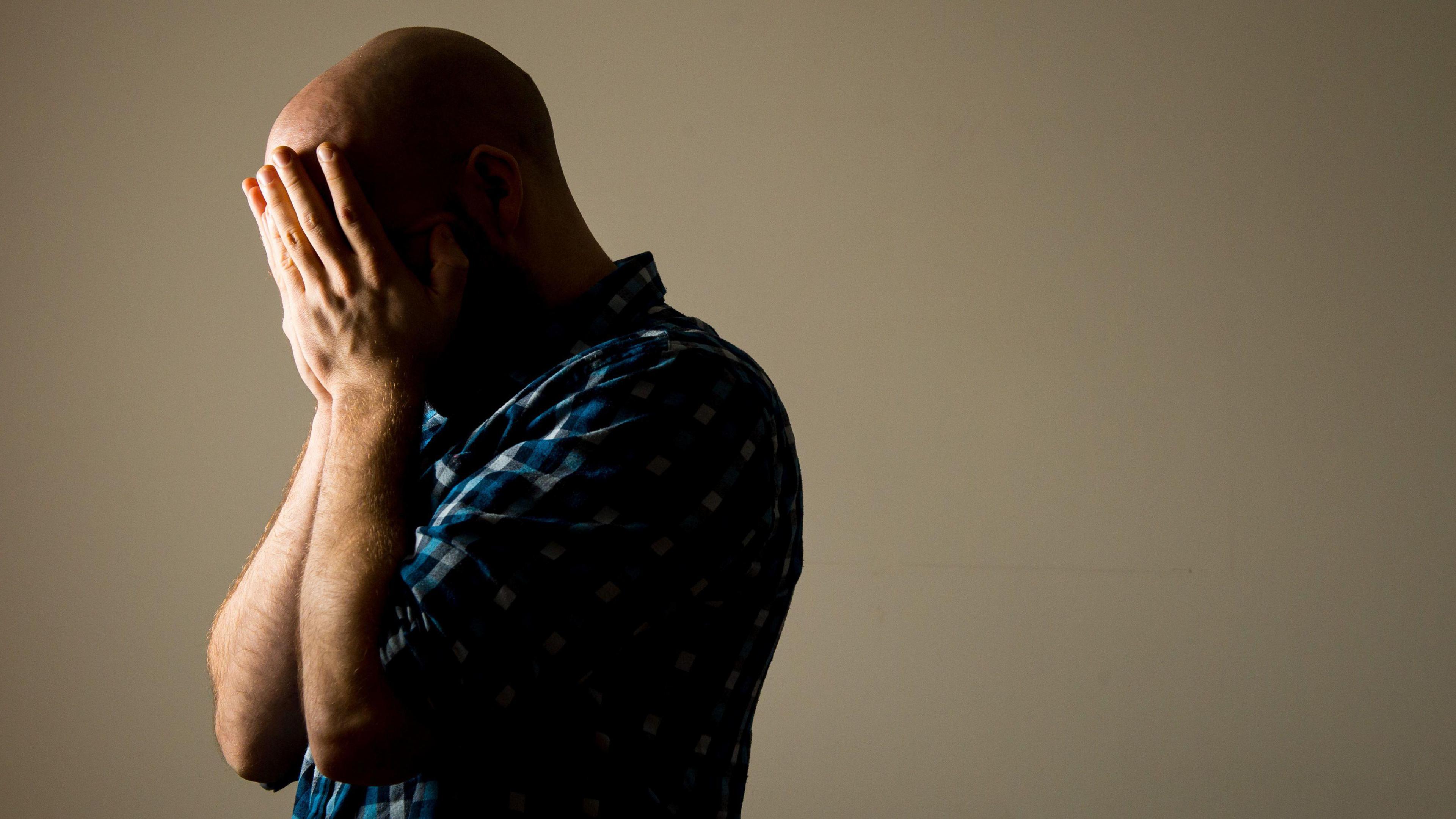 A bald man in a blue shirt holding his head in his hands 