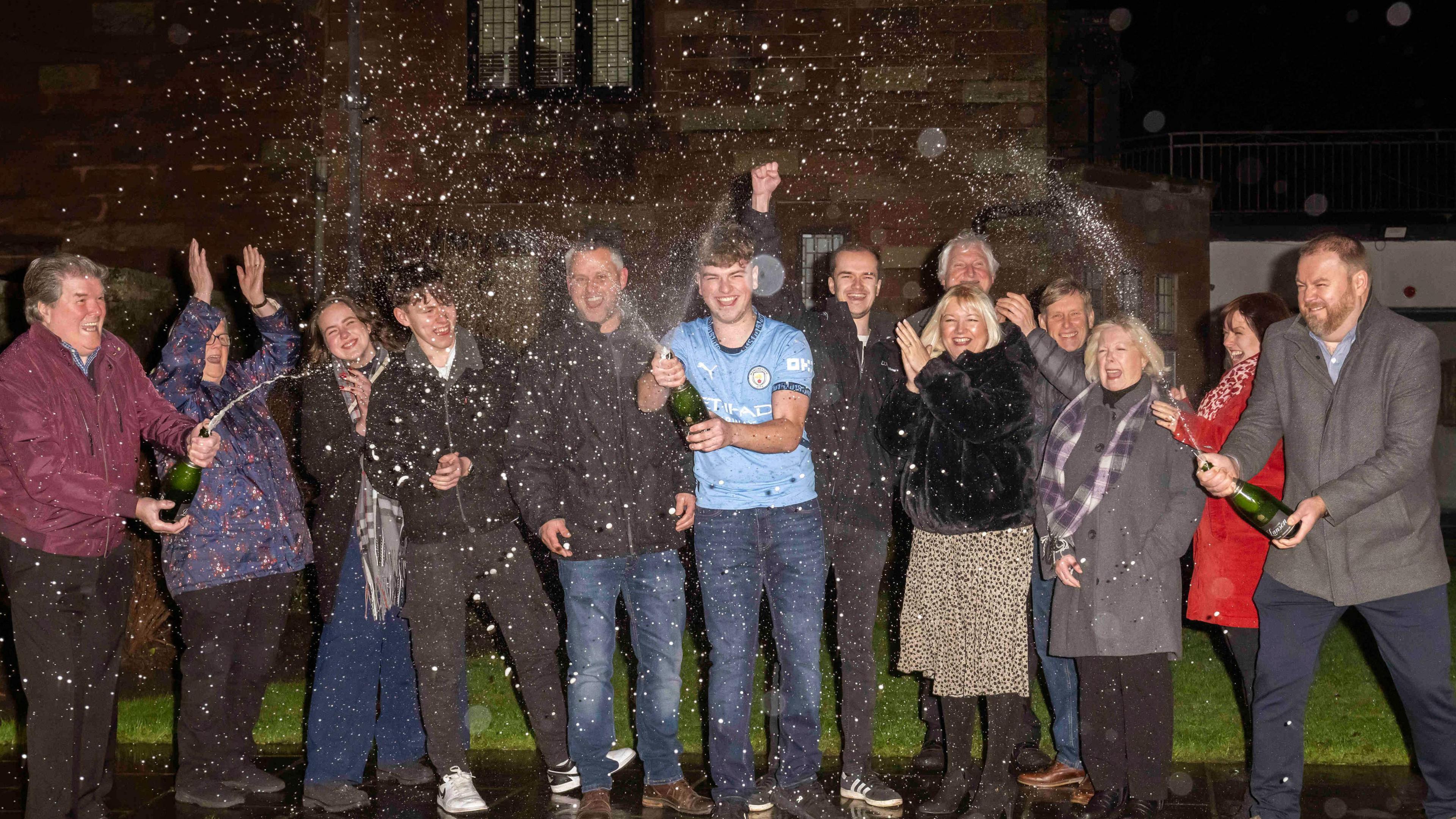 James Clarkson surrounded by family and friends, spraying champagne in a garden.