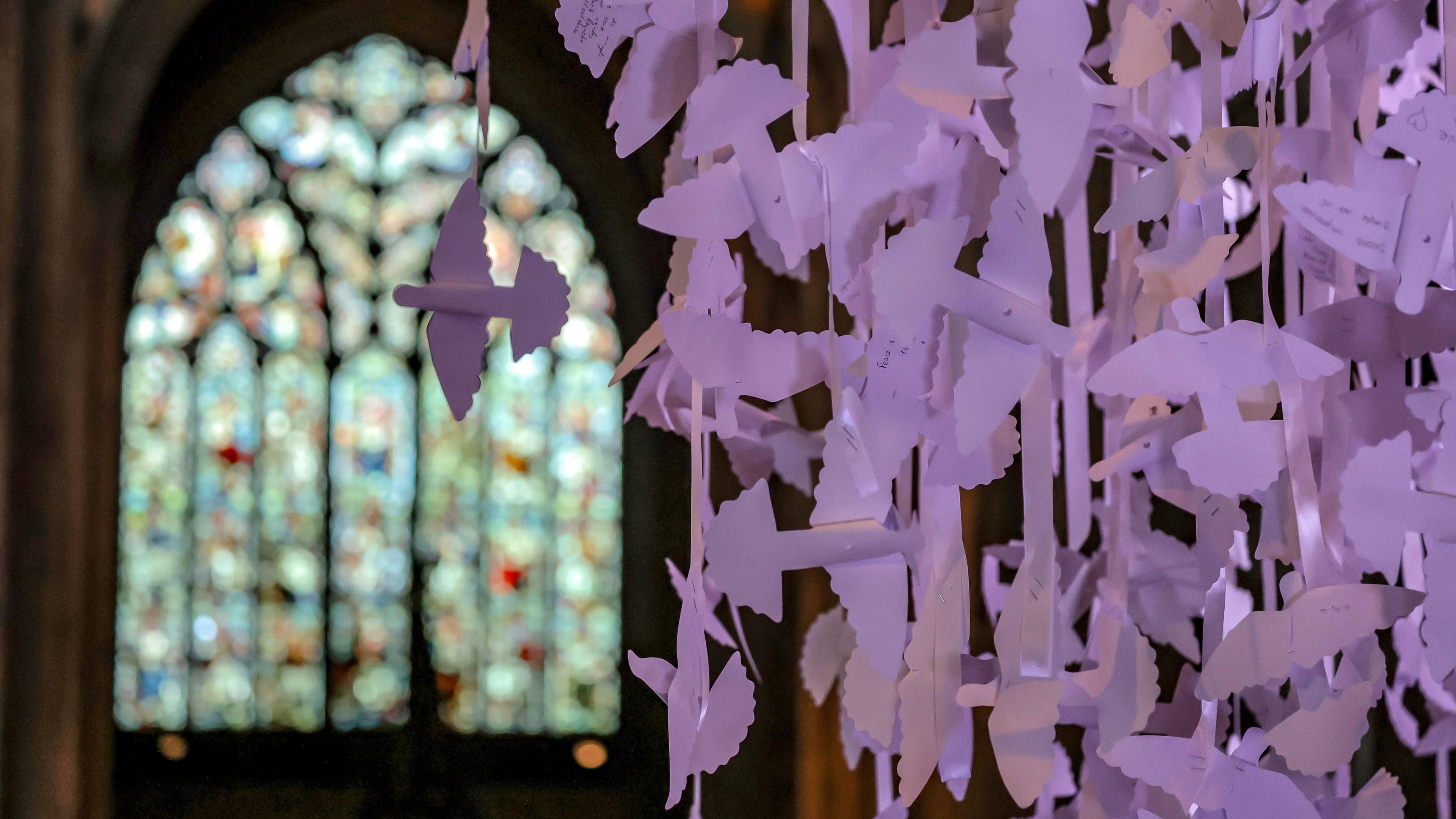 Close-up view of the white paper Peace Doves installation. One of the cathedral's stained glass windows is in the background.