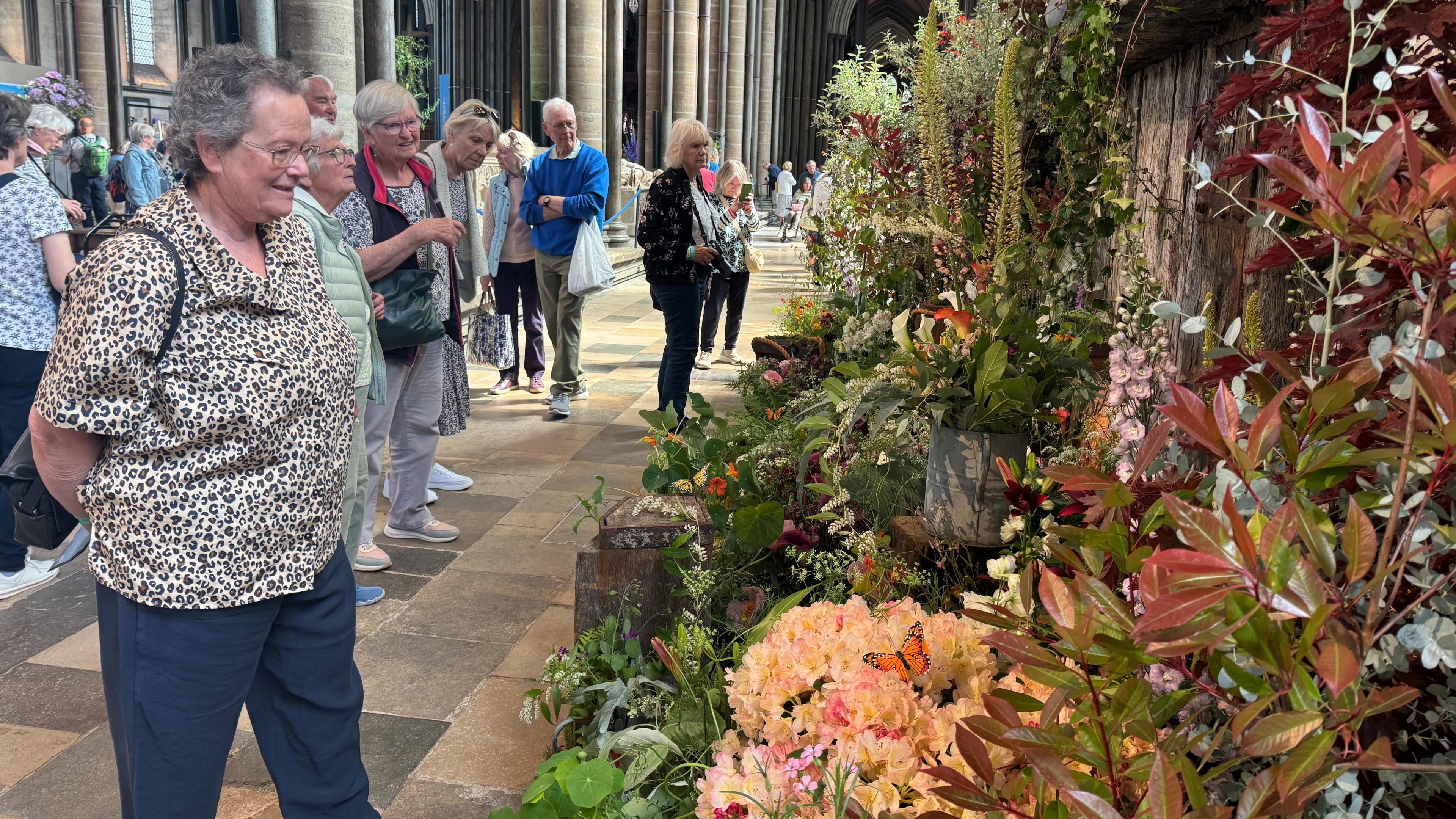 A lady looking on at a flower display to the right. The display is in an array of colours inside the cathedral.