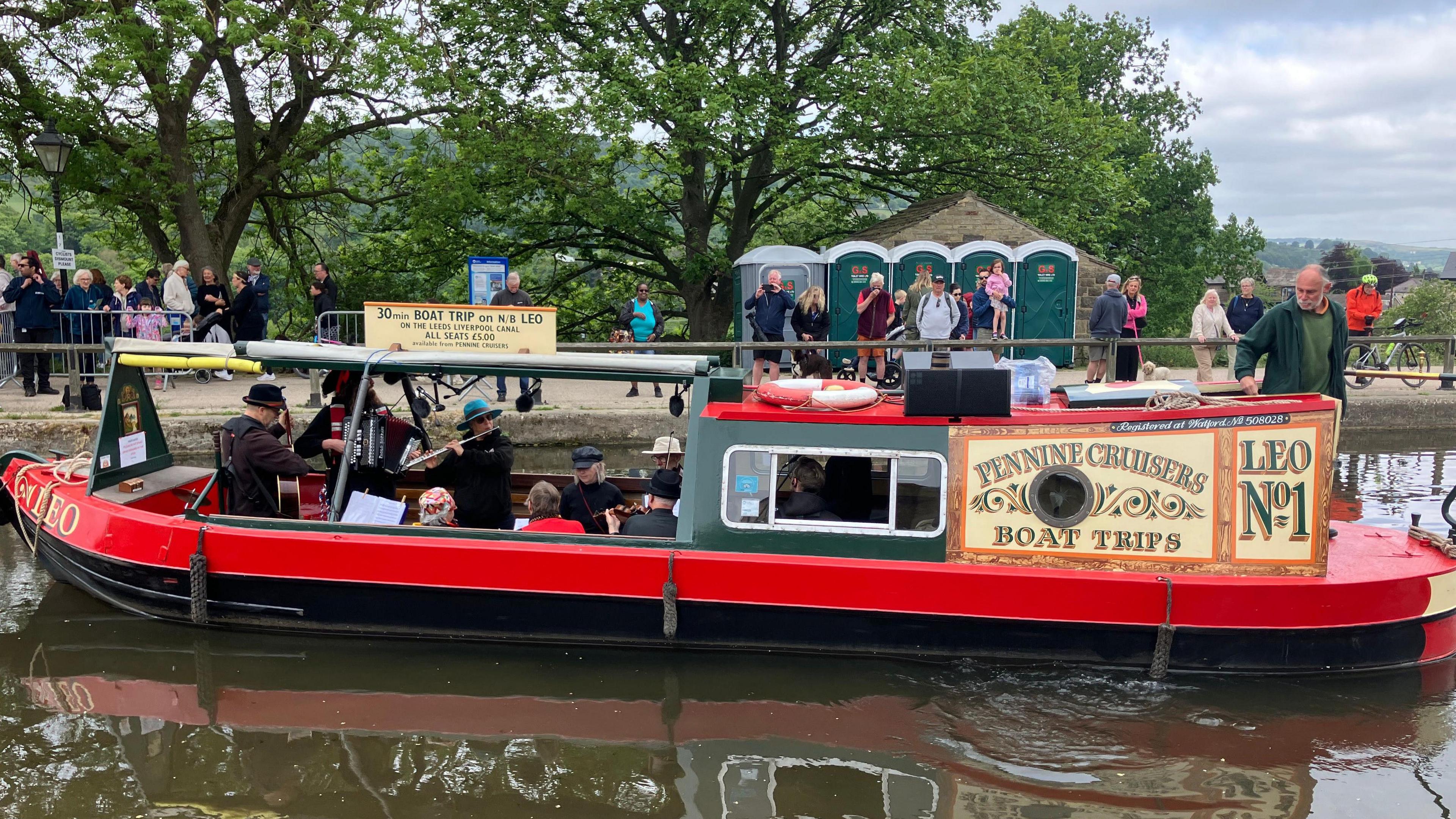 A canal boat with a group of musicians performing for the crowd in the background.
