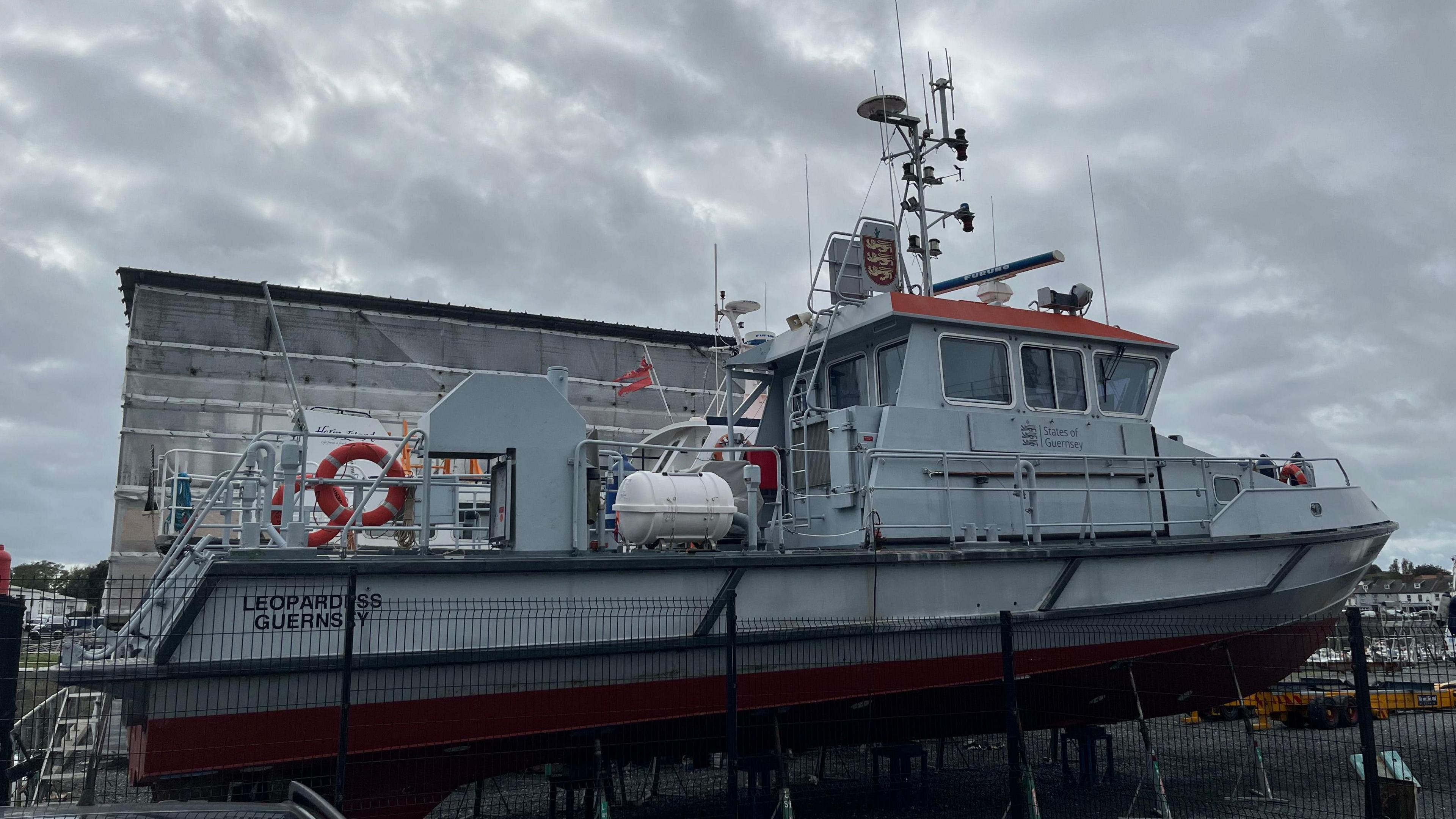 A grey ship, The Leopardess, behind a fence. It has the States of Guernsey logo on the side.