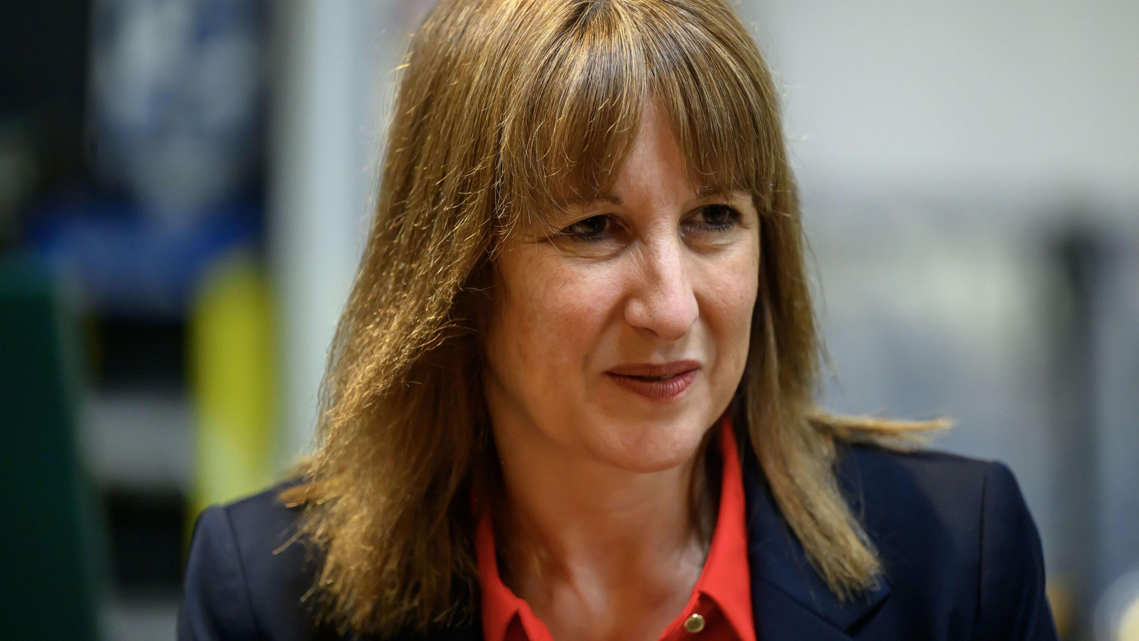 Chancellor Rachel Reeves wears a blue suit and red open necked shirt during a visit to the Sipsmith Distillery in Chiswick West London in October 2025.