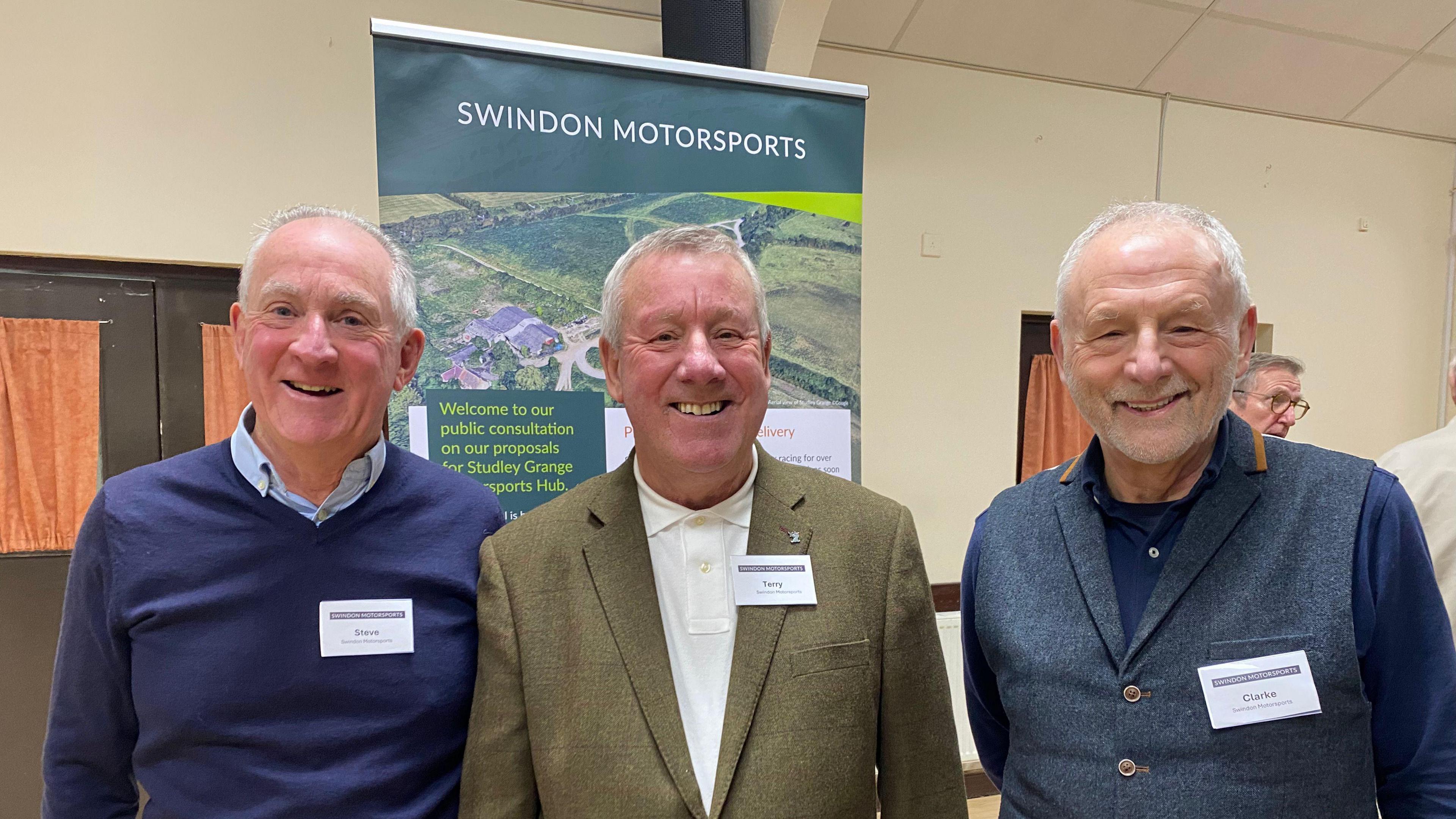 Steve Park, Terry Russell and Clarke Osborne - all involved in the scheme -  are standing in a hall in front of a banner with the plans. They are all smiling and looking into the camera. All are dressed smartly in shirts with name tags.