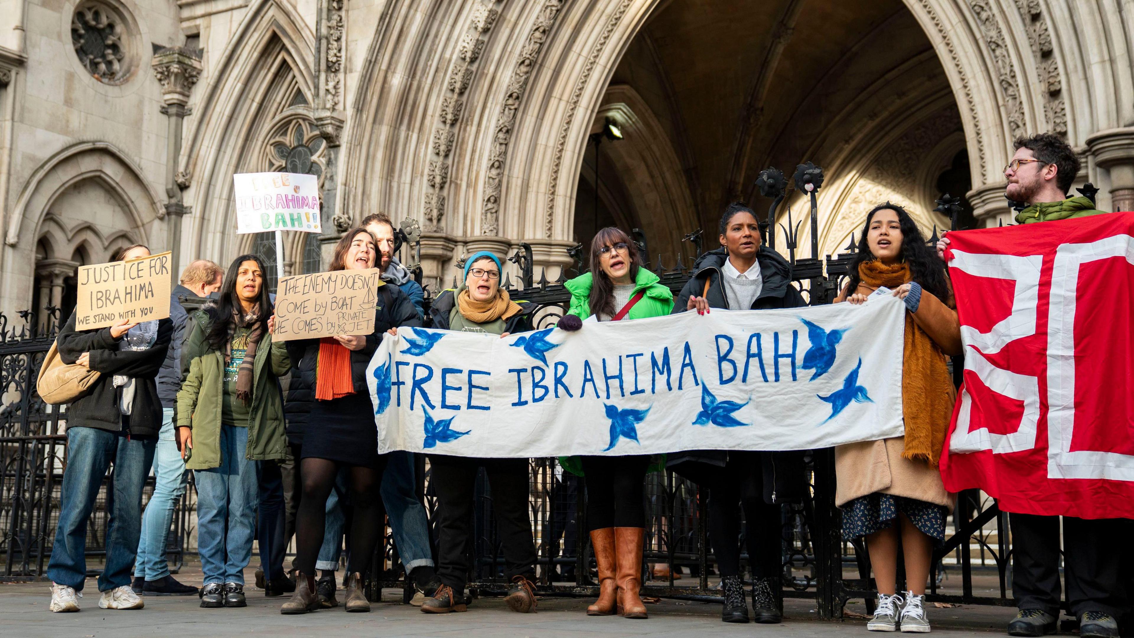 Protesters gathered outside the court house, holding banners. One says, "Free Ibrahima Bah". There are 10 people in the photo. 