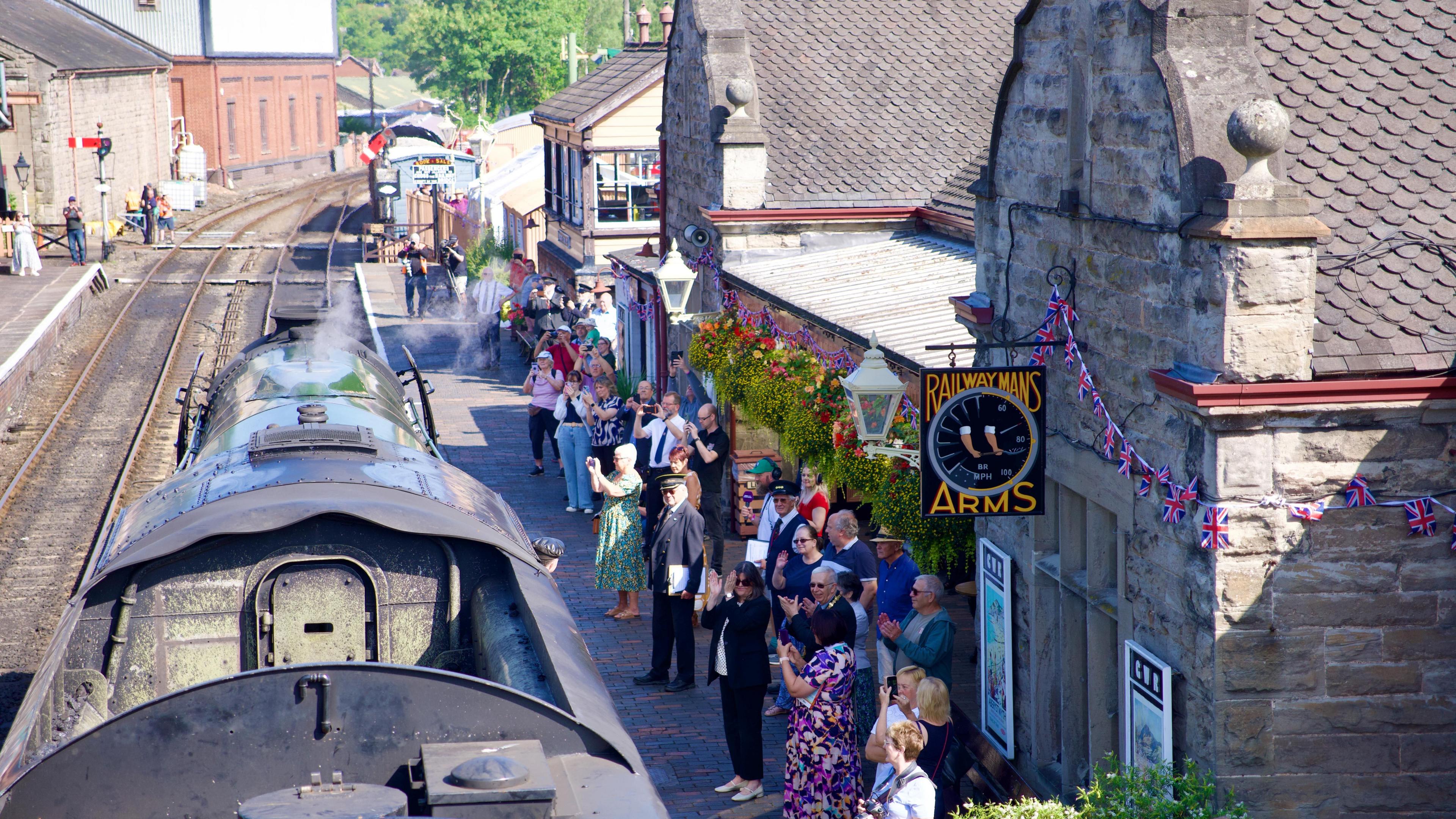 People stood on a railway platform, outside the Railwaymans Arms pub, greet the arrival of Flying Scotsman