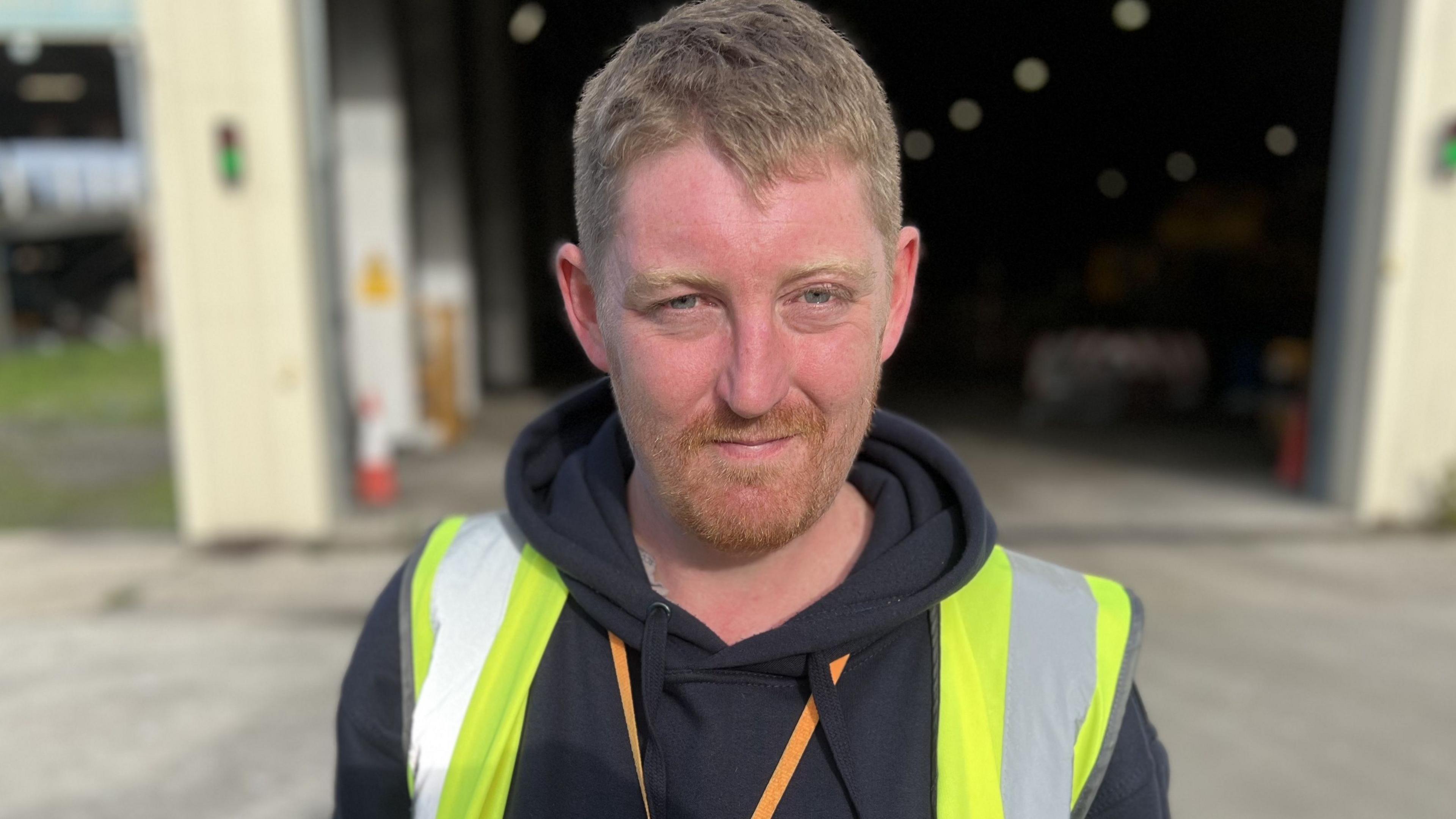 Waste warden Chris Smith wearing a black hoody and high visibility vest with short ginger hair and beard.