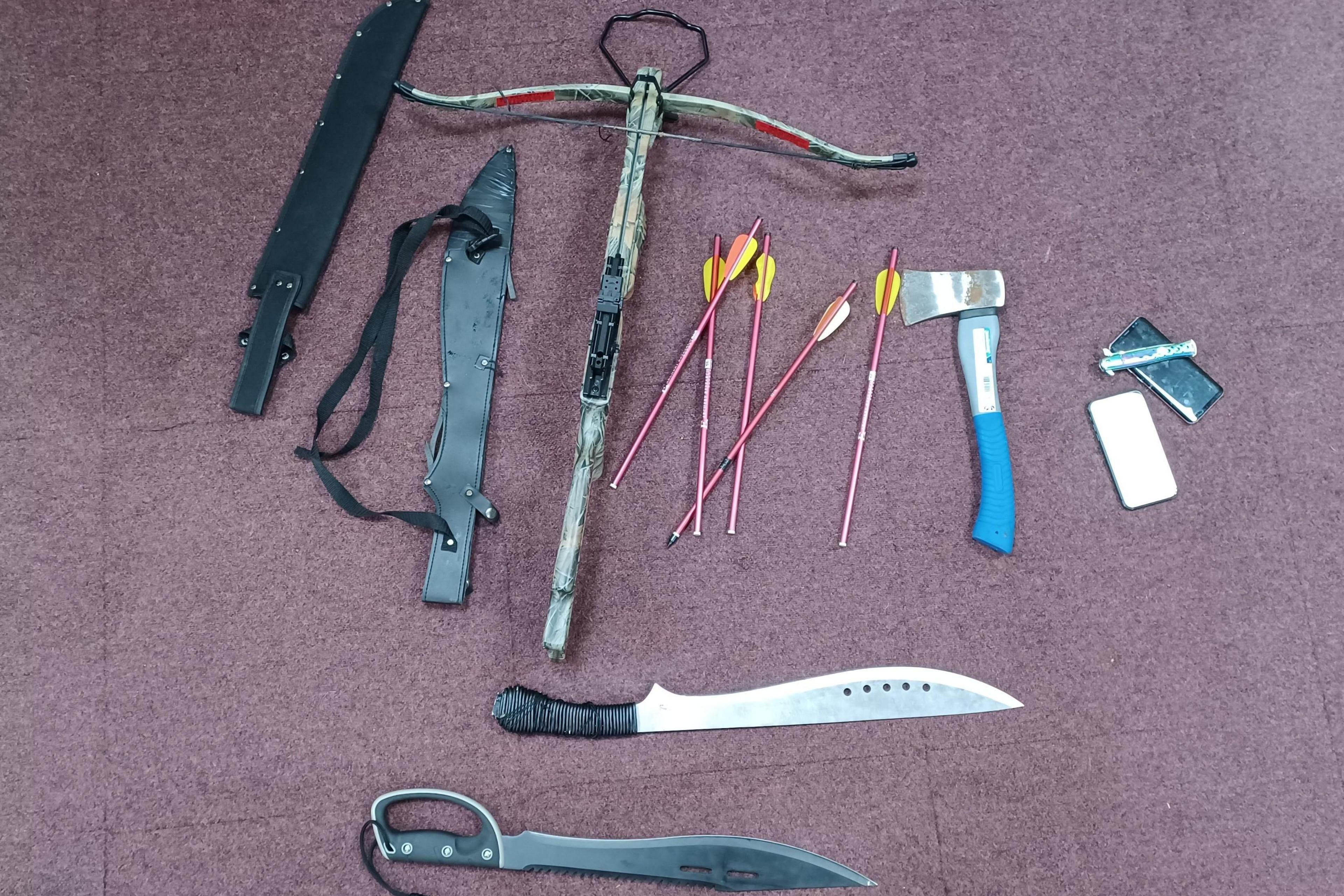 Weapons, including an axe, two large knives, a crossbow and darts, on a burgundy floor.