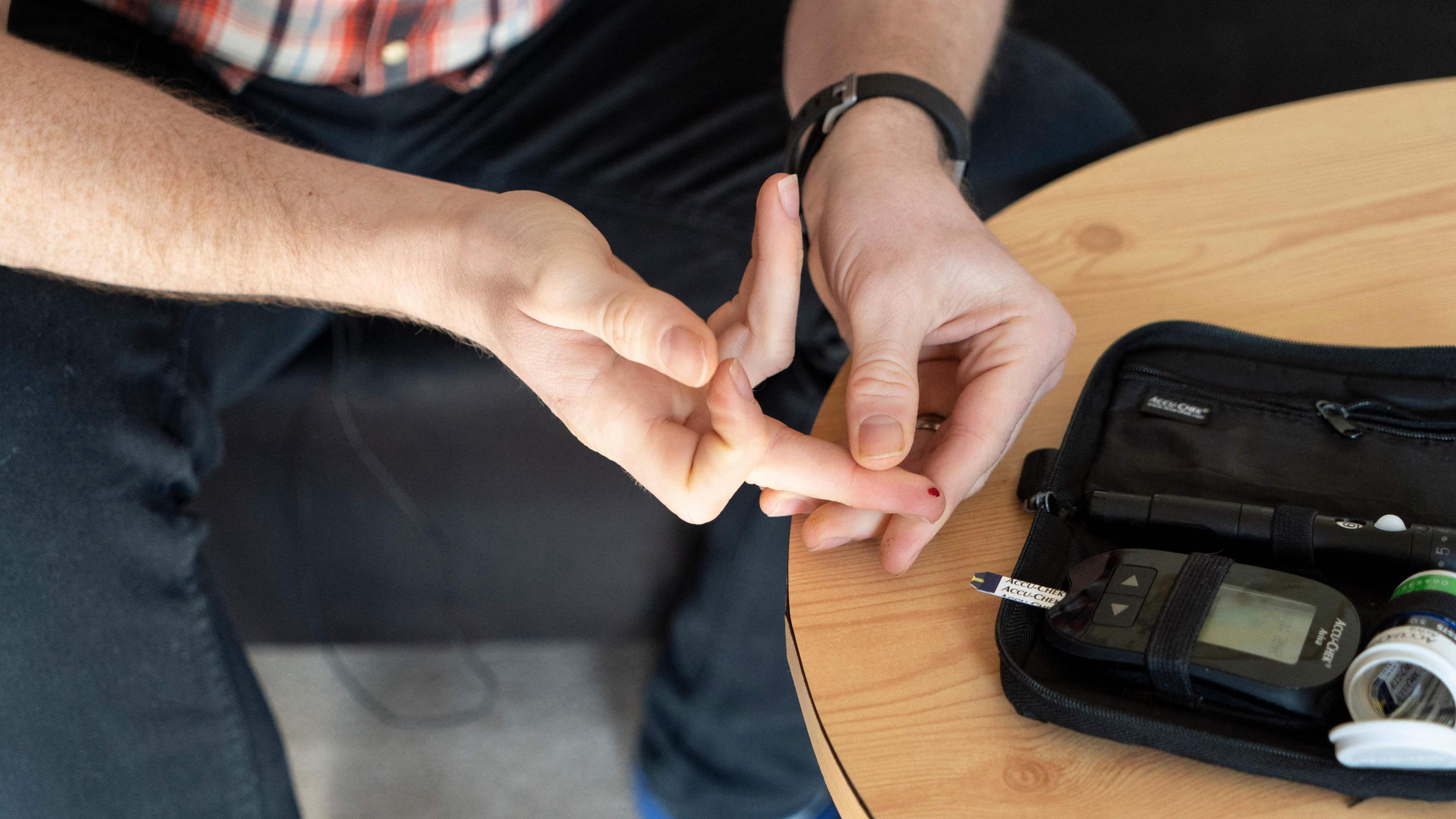 Picture of a man sitting down self-administering a blood test for diabetes using a machine 