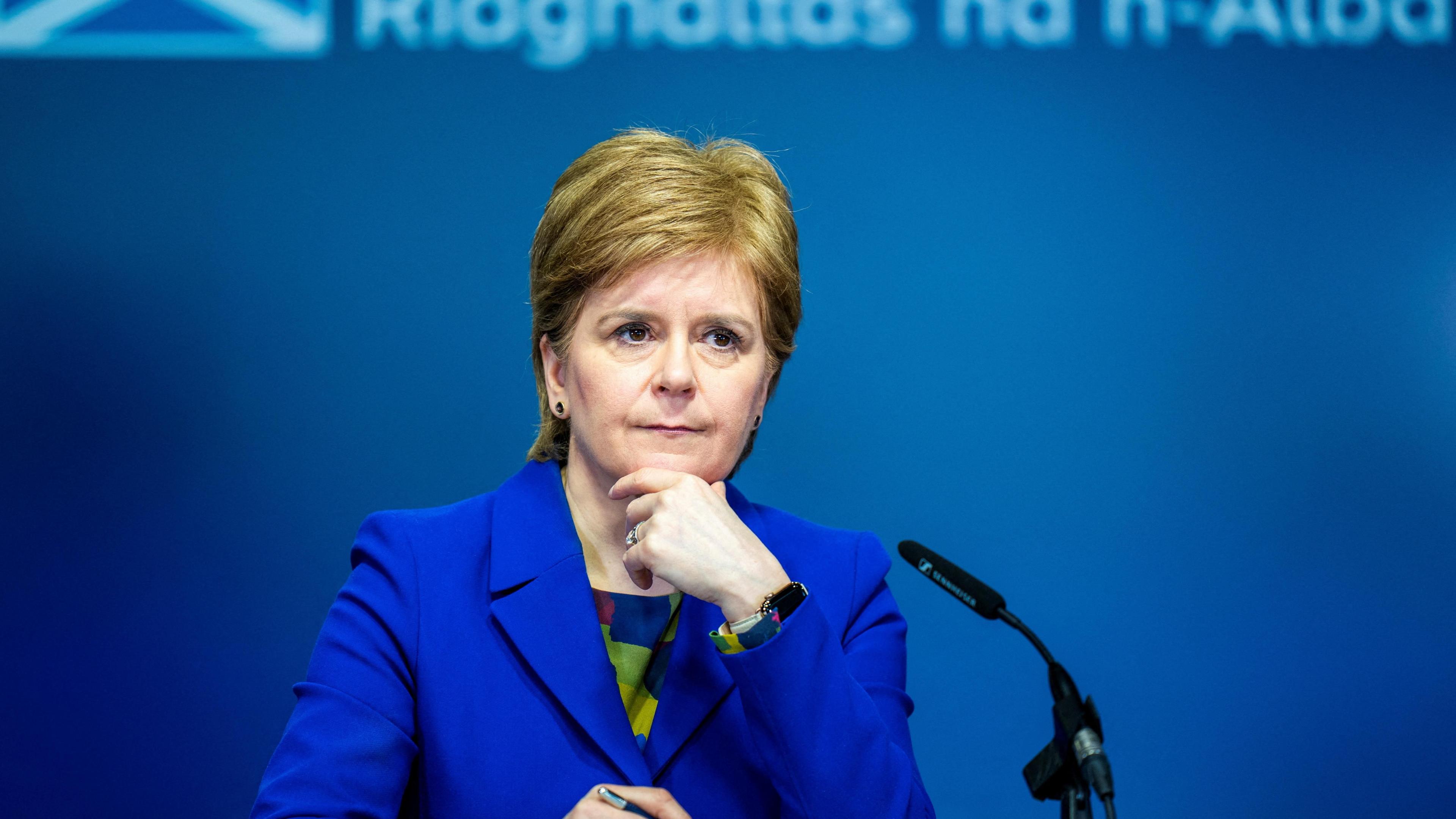 Nicola Sturgeon answering questions during a news conference at St Andrews House in Edinburgh in 2023. She is wearing a blue outfit and is standing in front of a blue background.