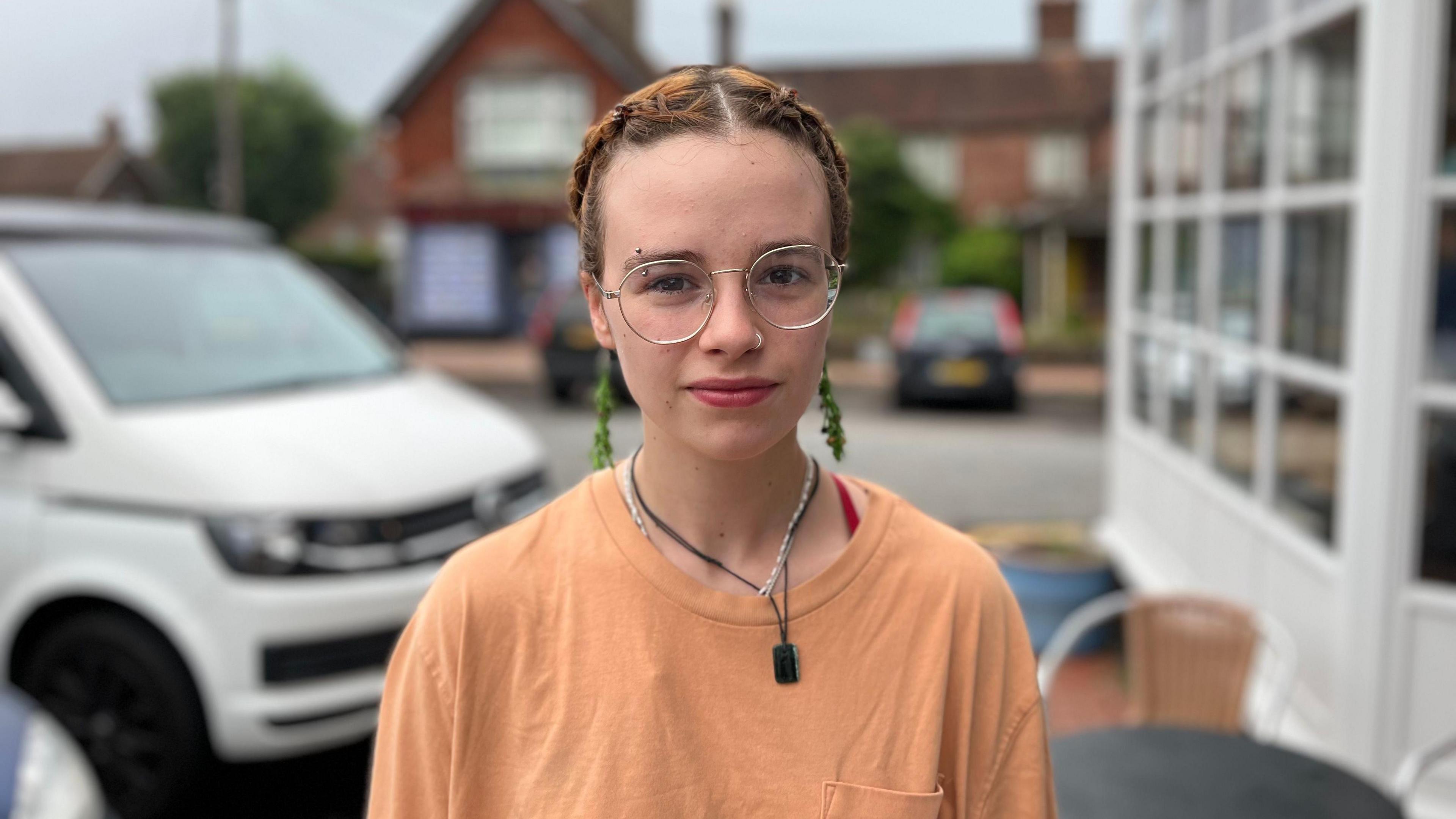 Annie Smith is in an orange t-shirt and with hair plaited close to her head, wearing glasses