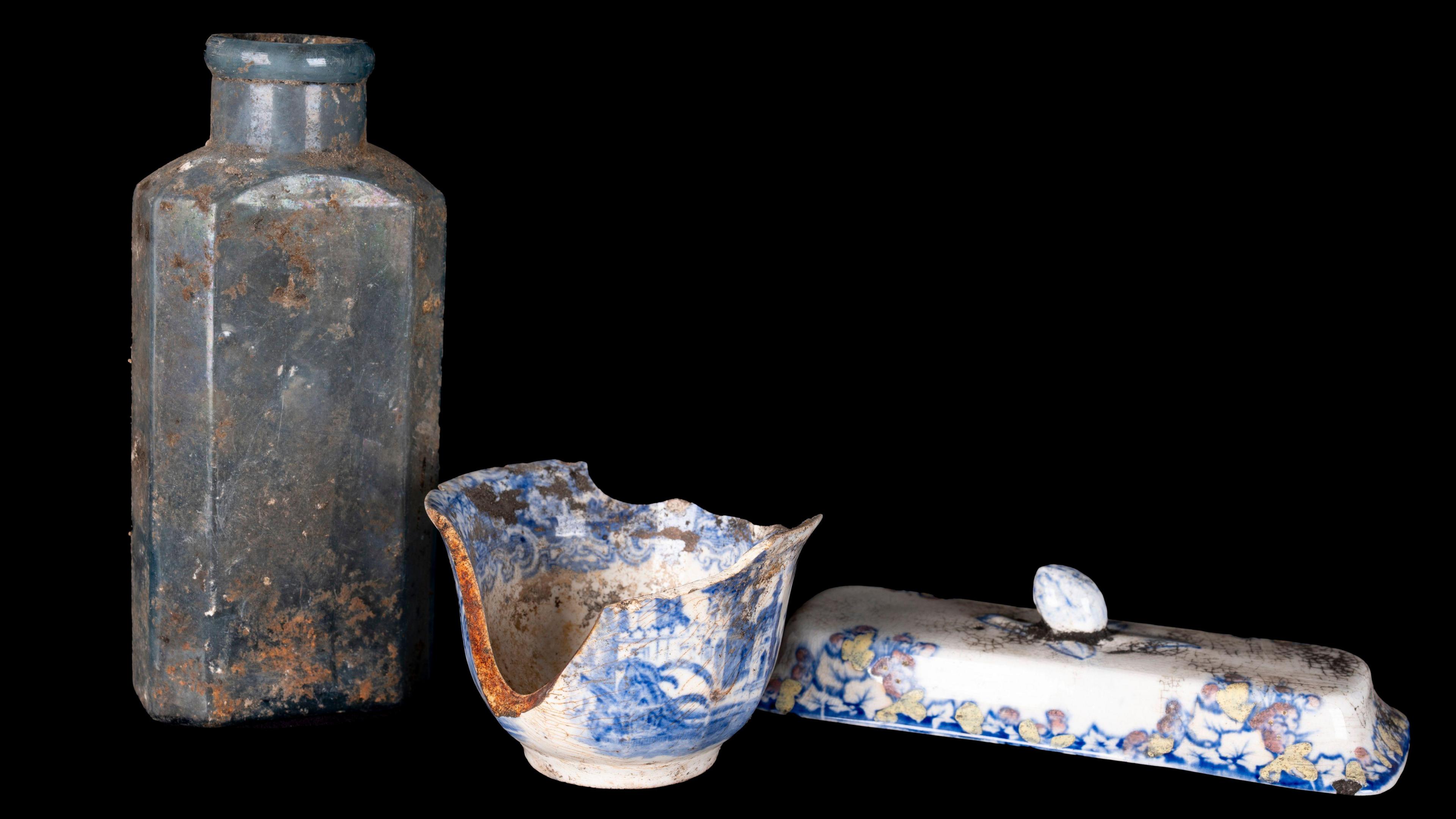 Opaque bottle on the left. A chipped bowl and the lid from a butter dish on the right. All against a black background.