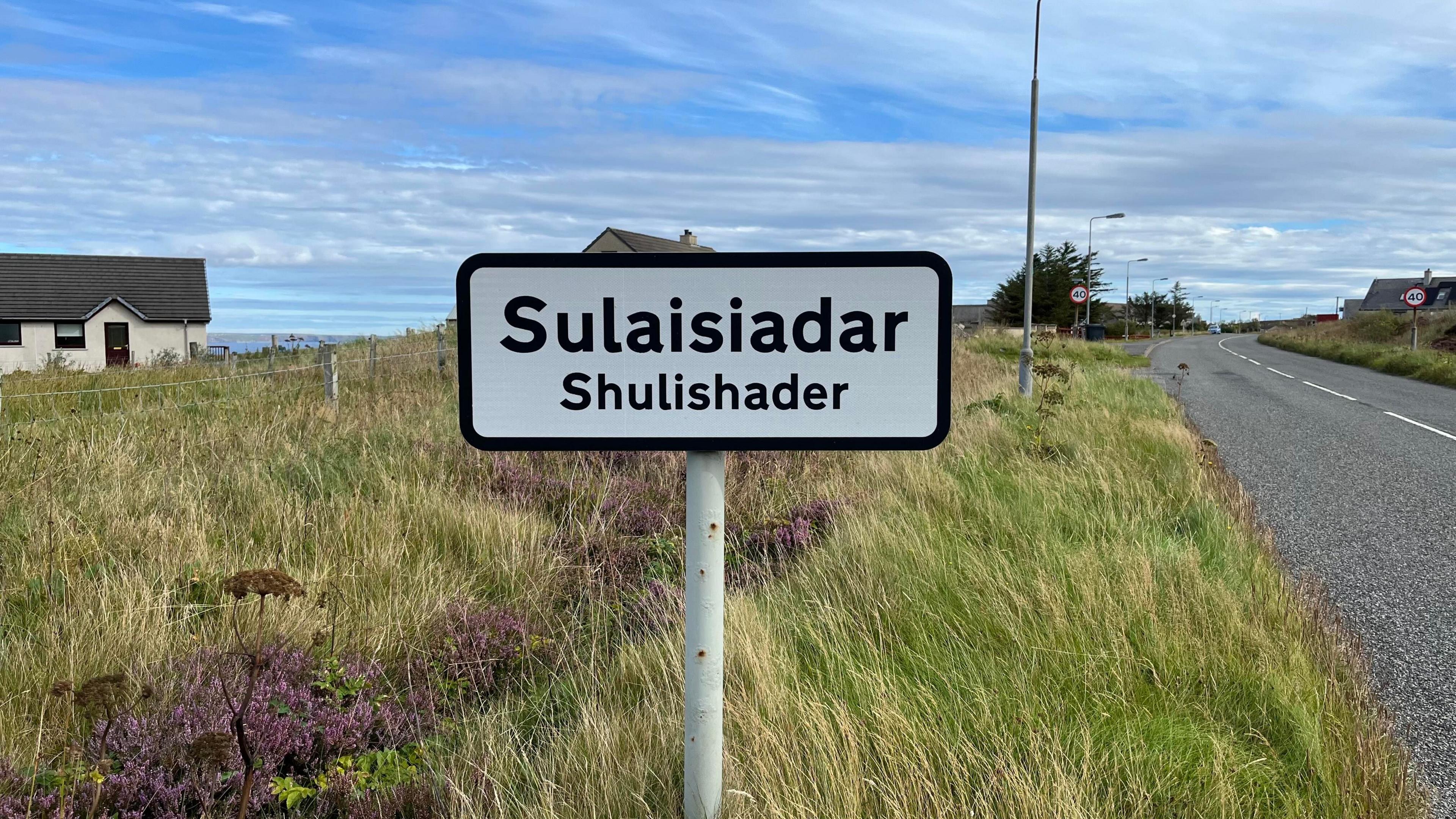 Dealbh de shoighne-rathaid baile Sulaisiadair air là breagha agus an adhar gorm.