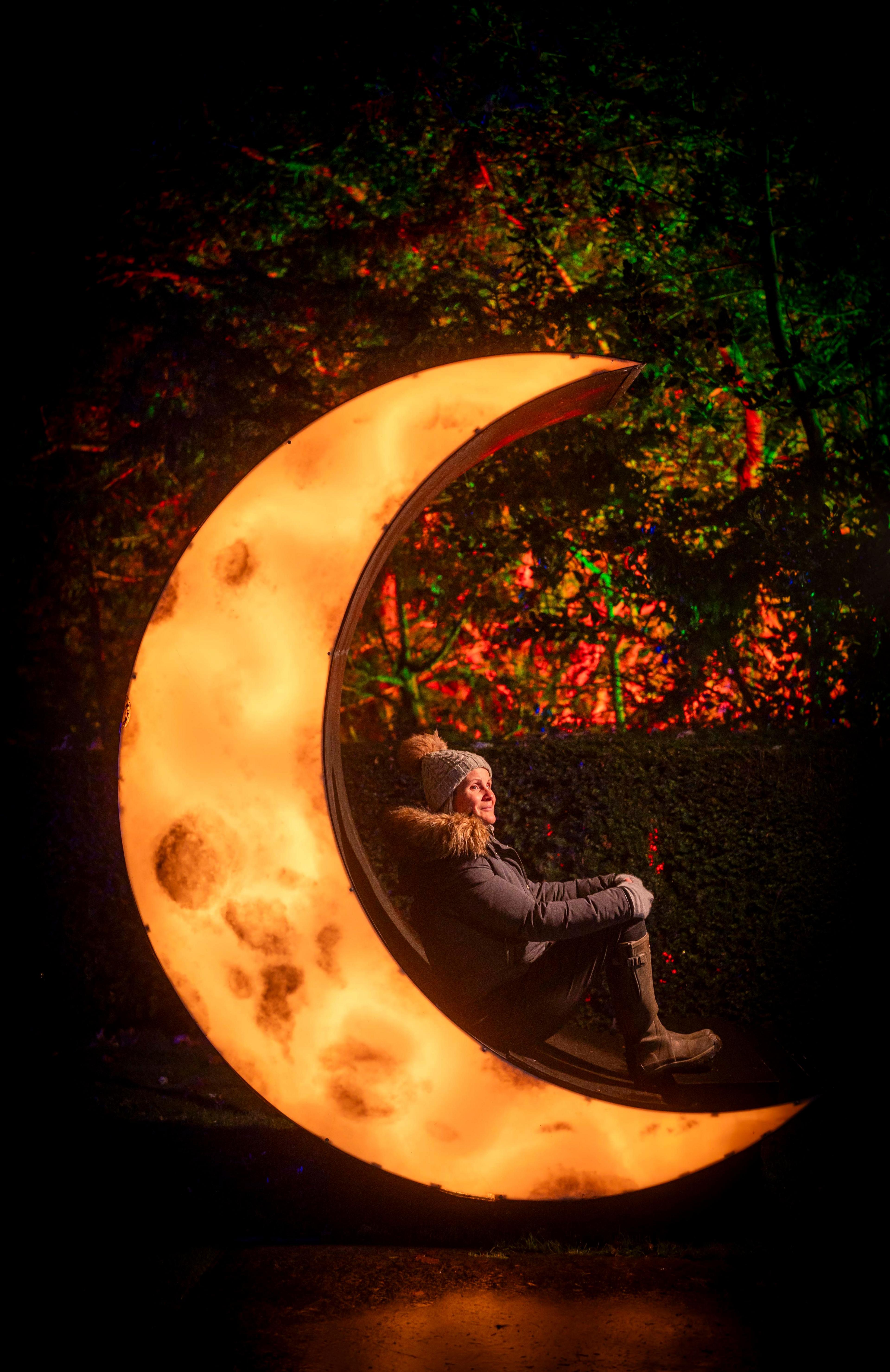 A woman in a hat sits on top of a moon-shaped light display