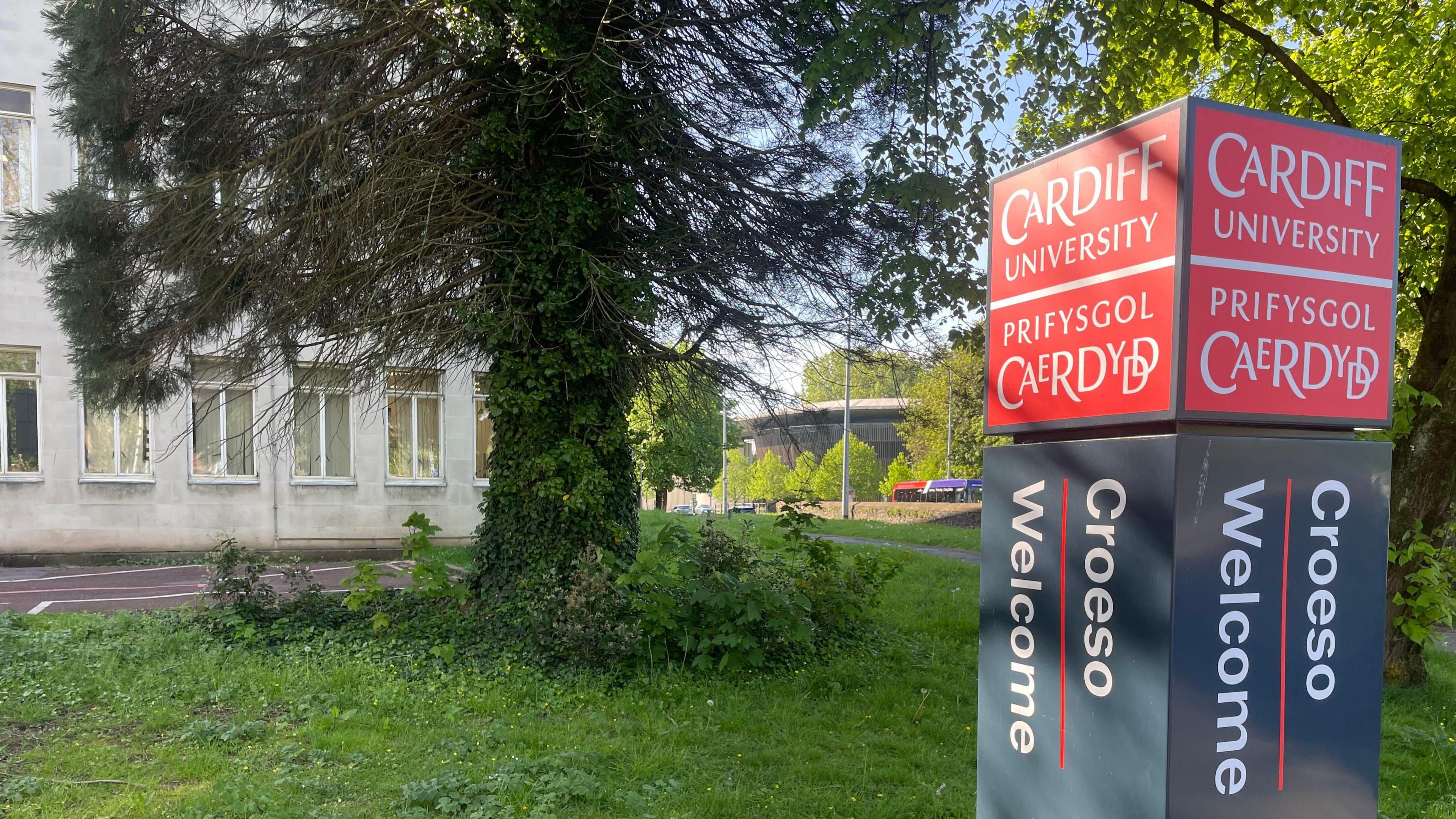 Mae arwydd yn nodi “Cardiff University / Prifysgol Caerdydd”, gyda “Croeso / Welcome” oddi tano.
