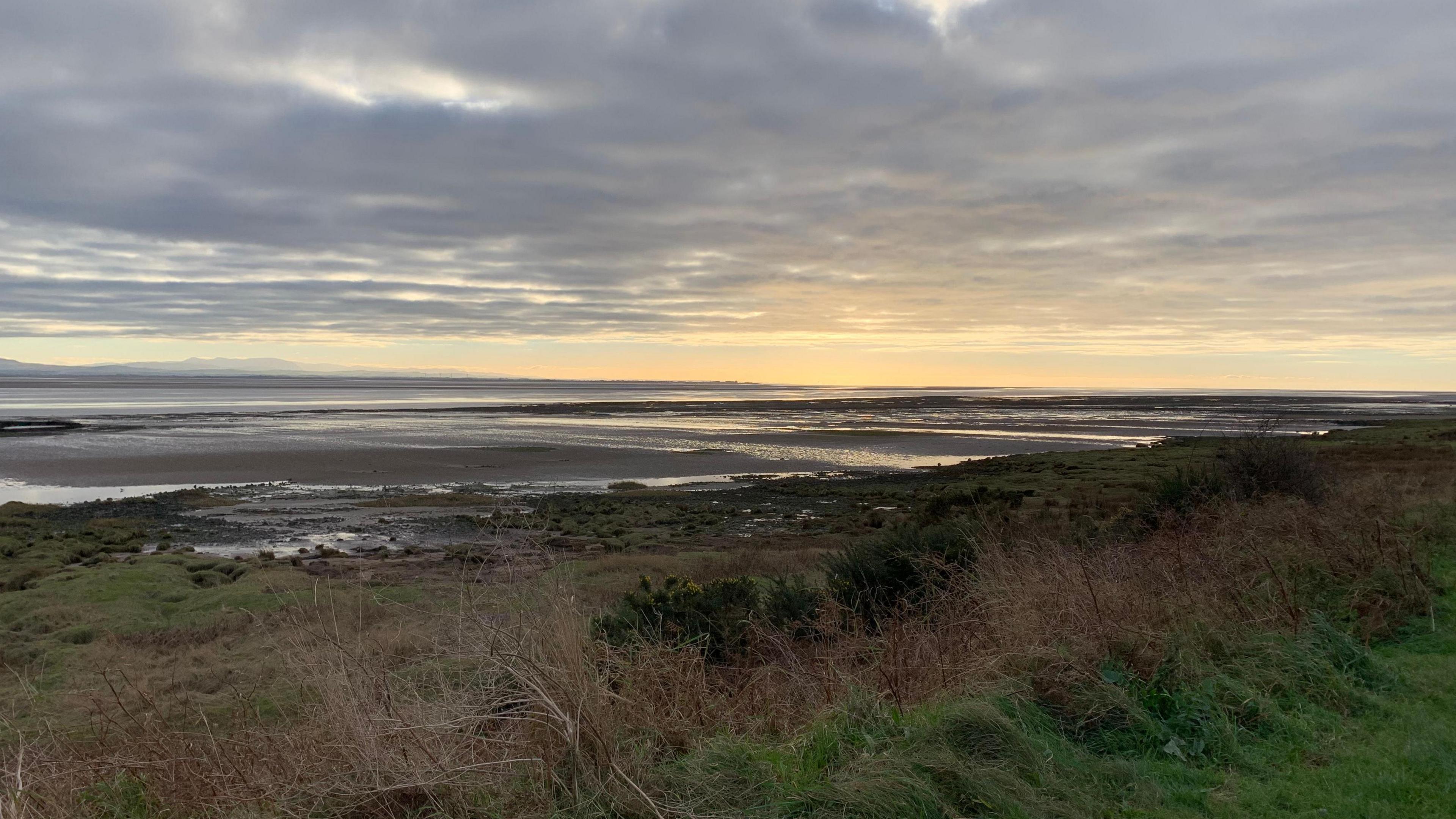 Solway estuary with beach/mudlats and an orange sky with grass in the foreground