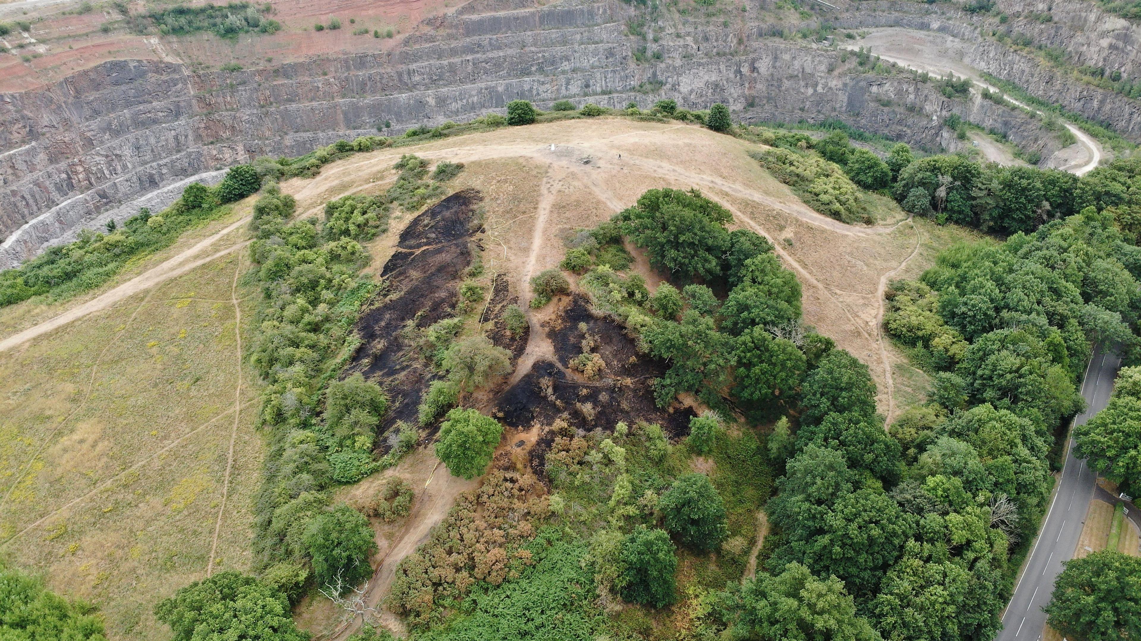 Ariel view of the aftermath of the large grassland fire at Croft Hill, Leicestershire, showing the damaged area, which is surrounded by green trees and open space.