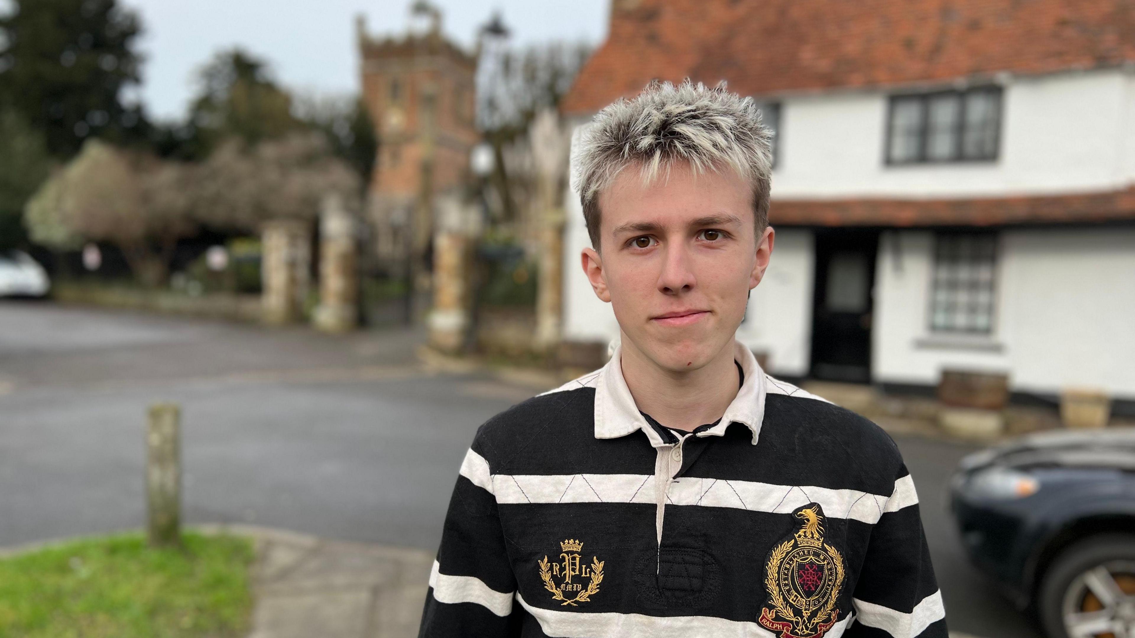 The foreground, Fletcher Rodger wearing a black and white striped shirt smiles at the camera with St Mary's Church behind him