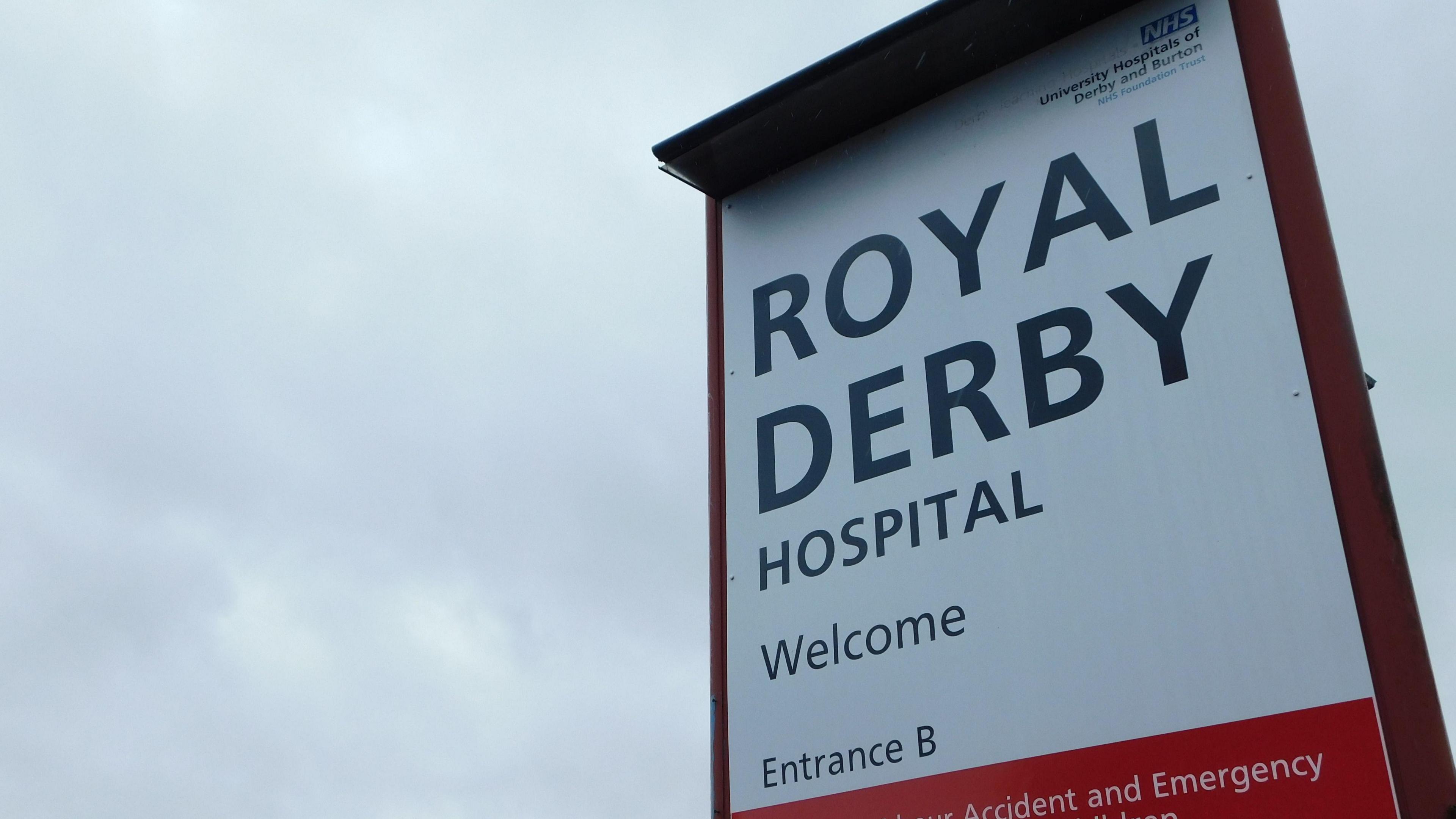 A close-up photograph of a sign at the Royal Derby Hospital saying "welcome Entrance B" with a cloudy sky behind 