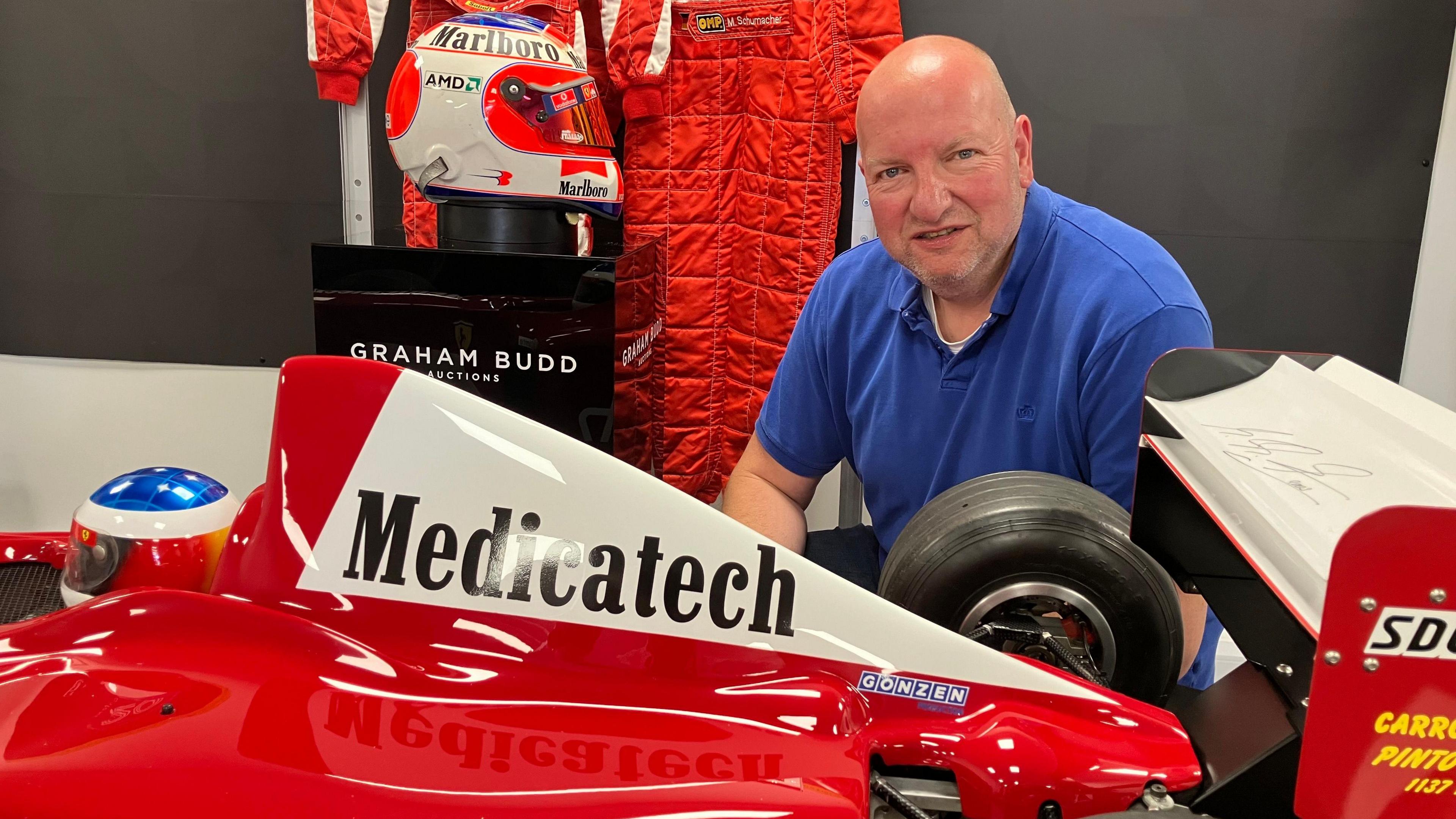 Man in blue polo shirt kneeling in front of red ferrari replica