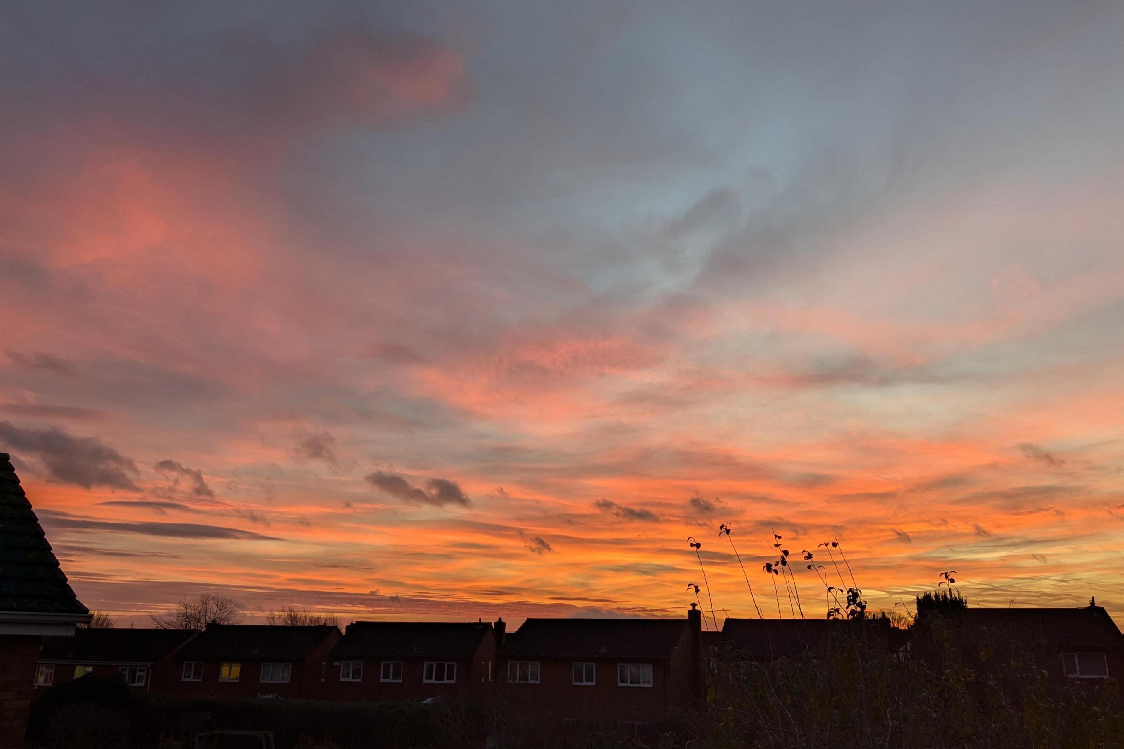 An orange and light blue sky is seen above the rooftops. Virtually all the lights are off in the houses at the bottom of the image.