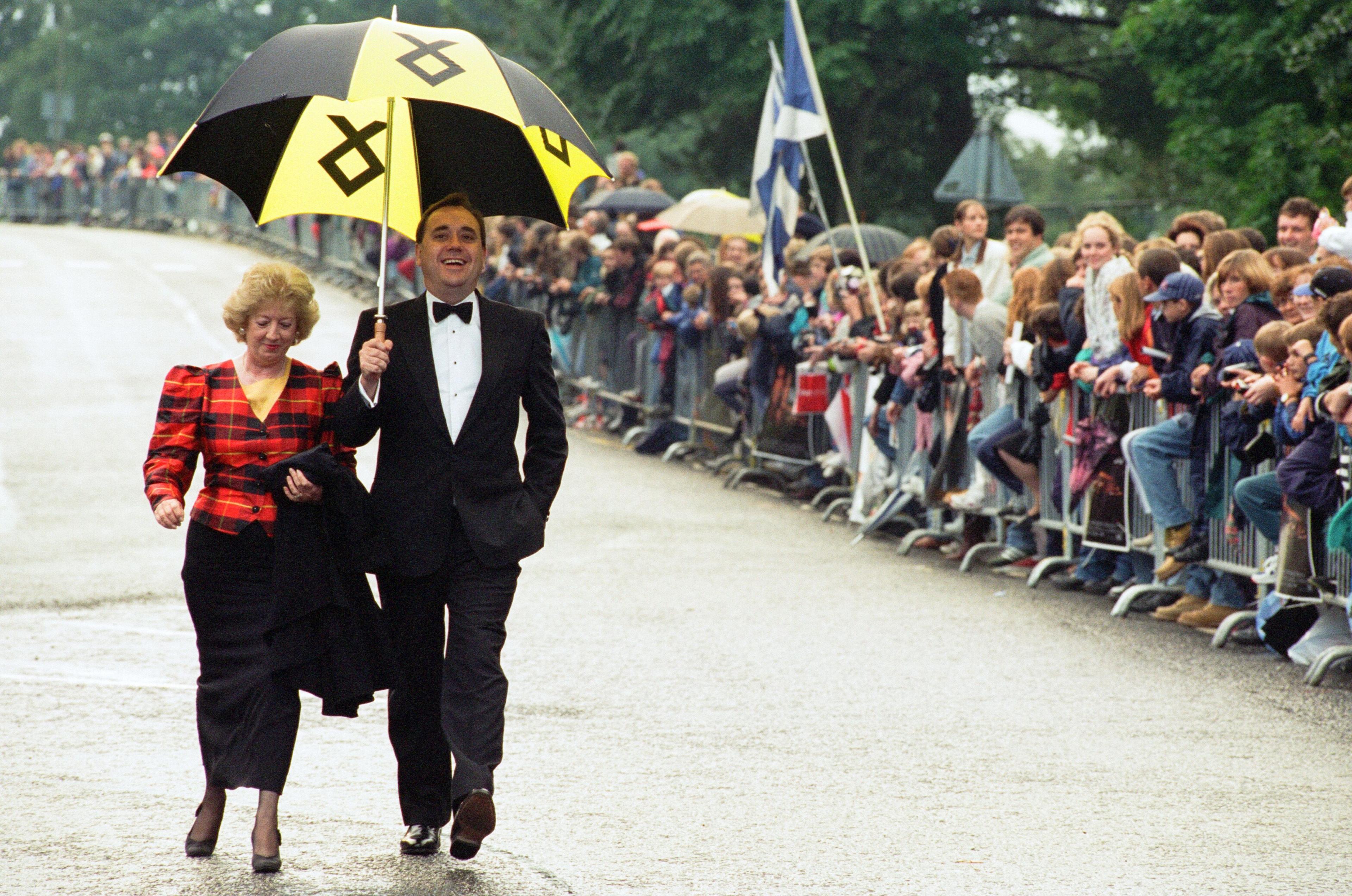 Alex Salmond pictured with his wife Moira at the Braveheart premiere in Stirling in 1995. Moira wears a tartan blazer while Alex wears a black suit jacket, white shirt and black bowtie. He is carrying a black and yellow umbrella.