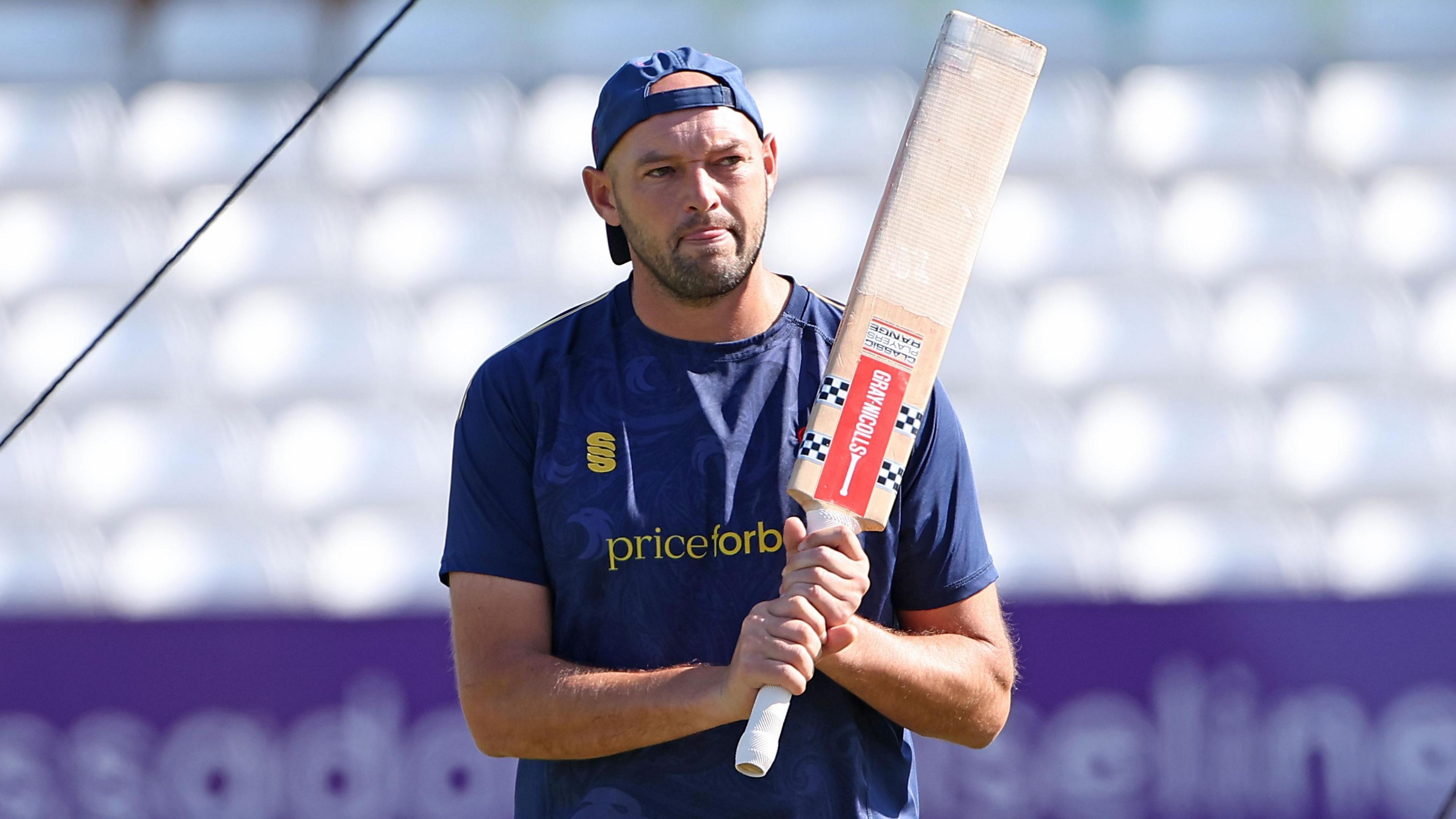 Nick Browne stands with his Essex cap on backwards with his bat resting against his left shoulder during a warm-up session