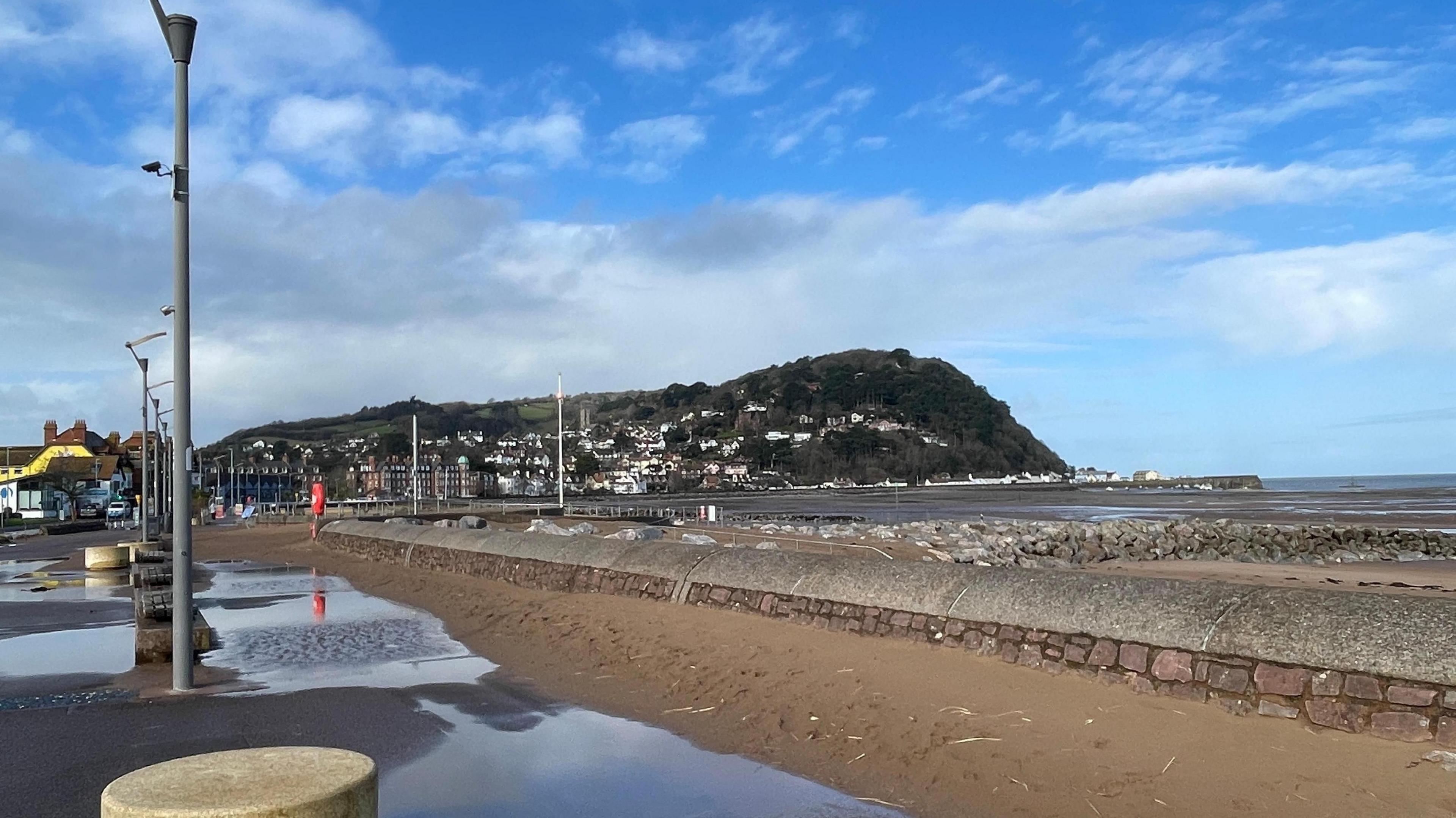 Puddles to left of a beach scene with blue skies above. 