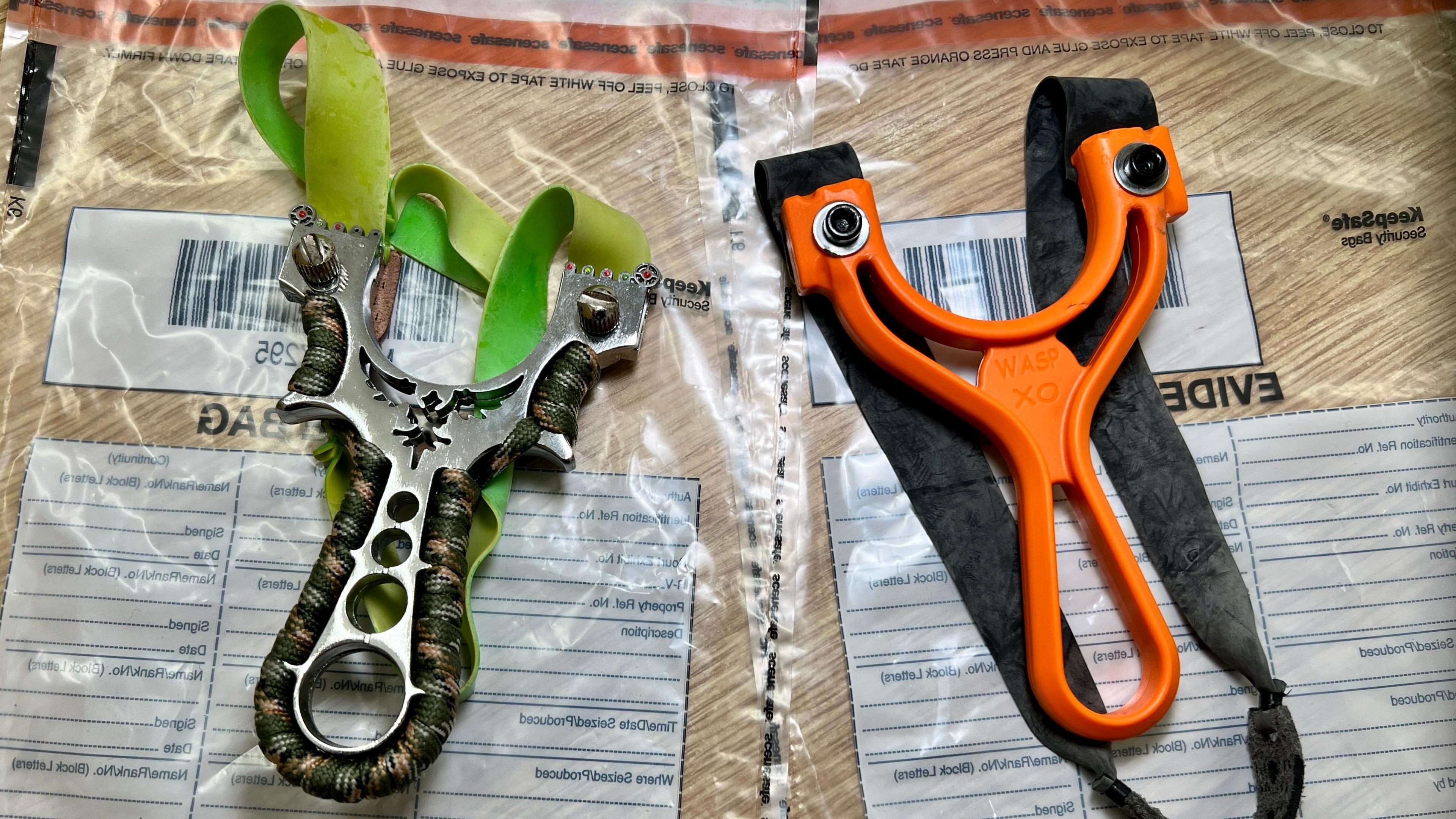 Two catapults sit on top of police evidence bags.