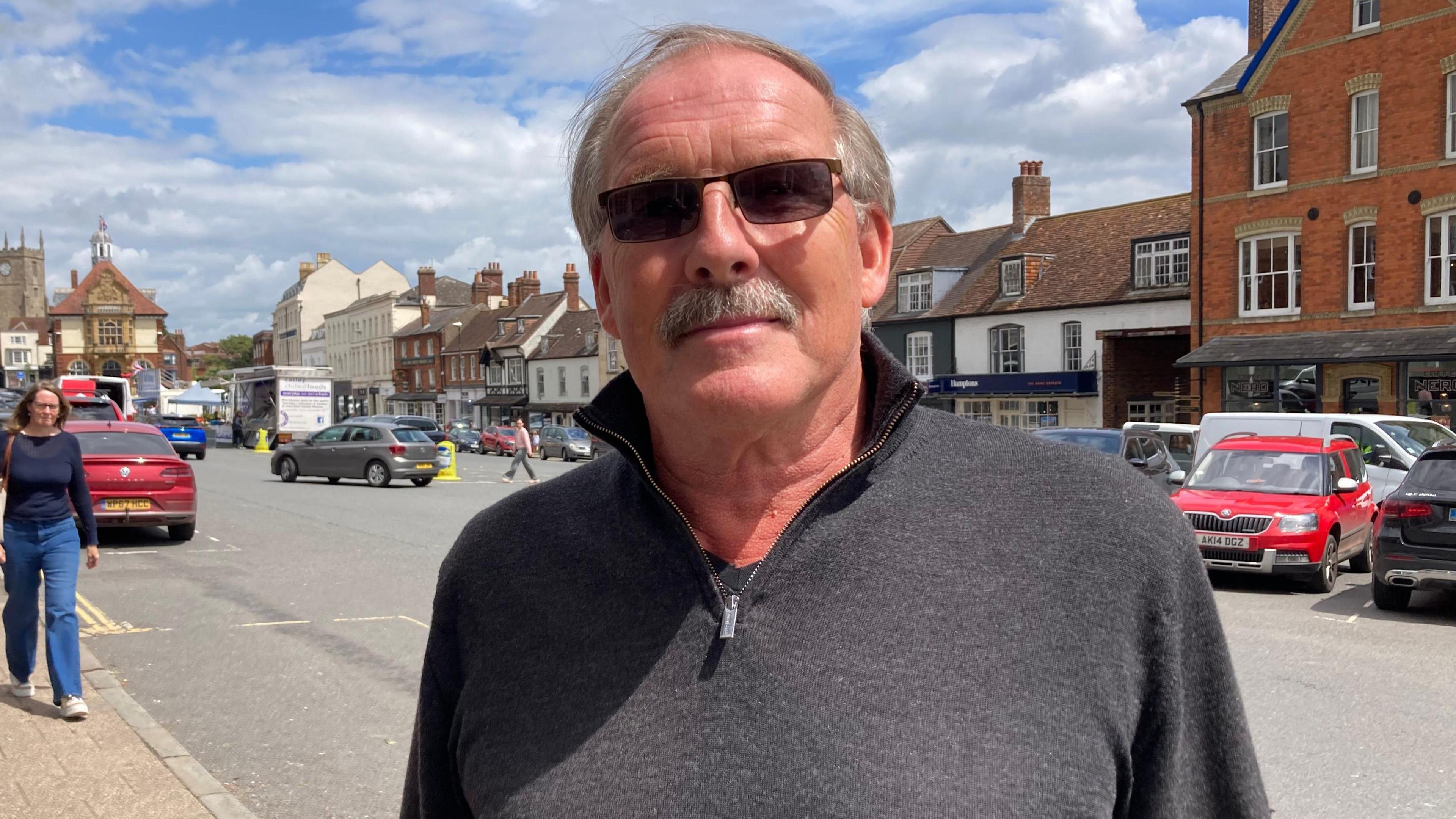 Gary Farrow. He is pictured in Marlborough town centre. He has short grey hair and a grey moustache. He is wearing dark square-shaped sunglasses.