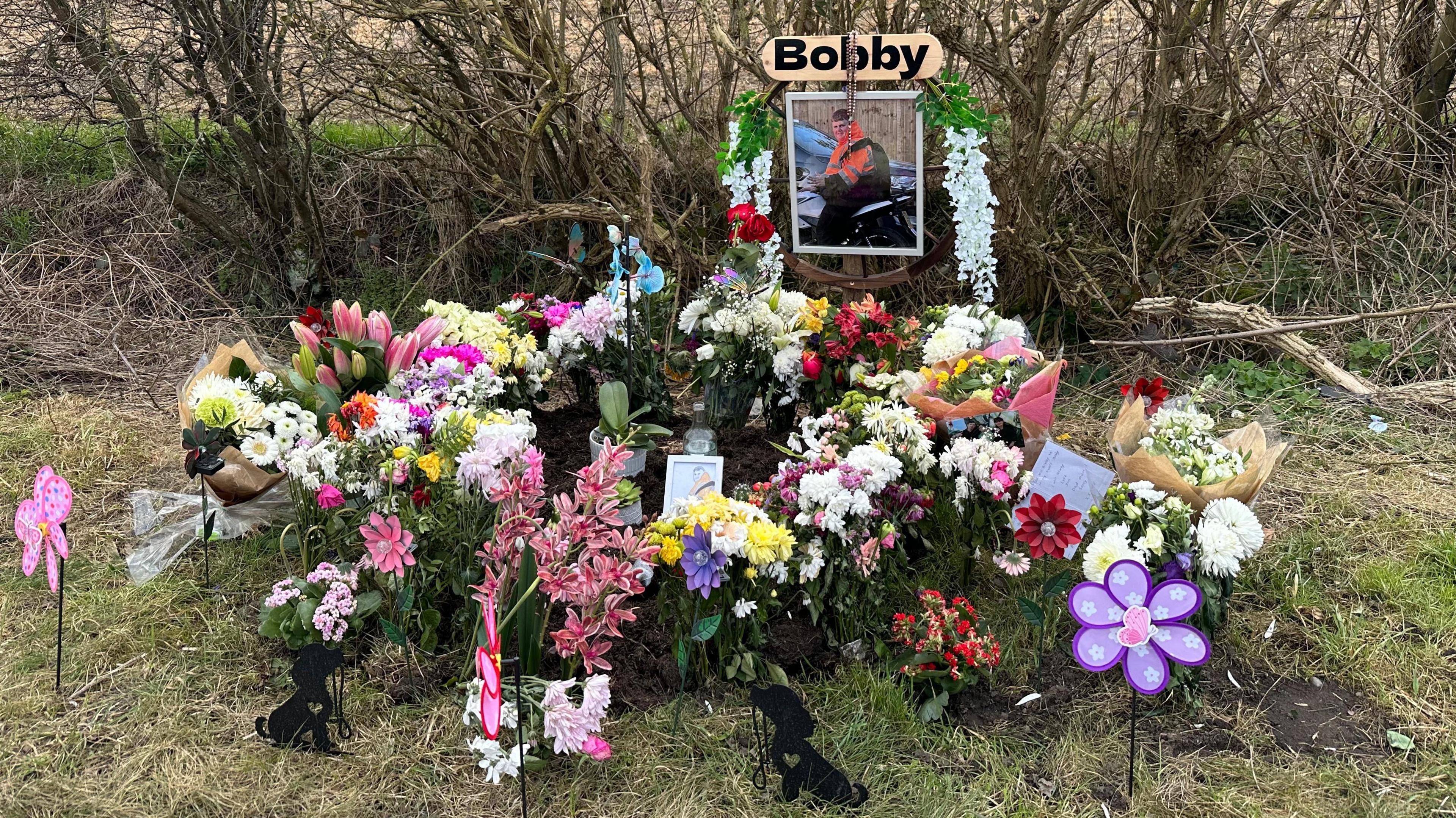 Flowers, photos and tributes left on the side of the road at the site of a traffic collision. 