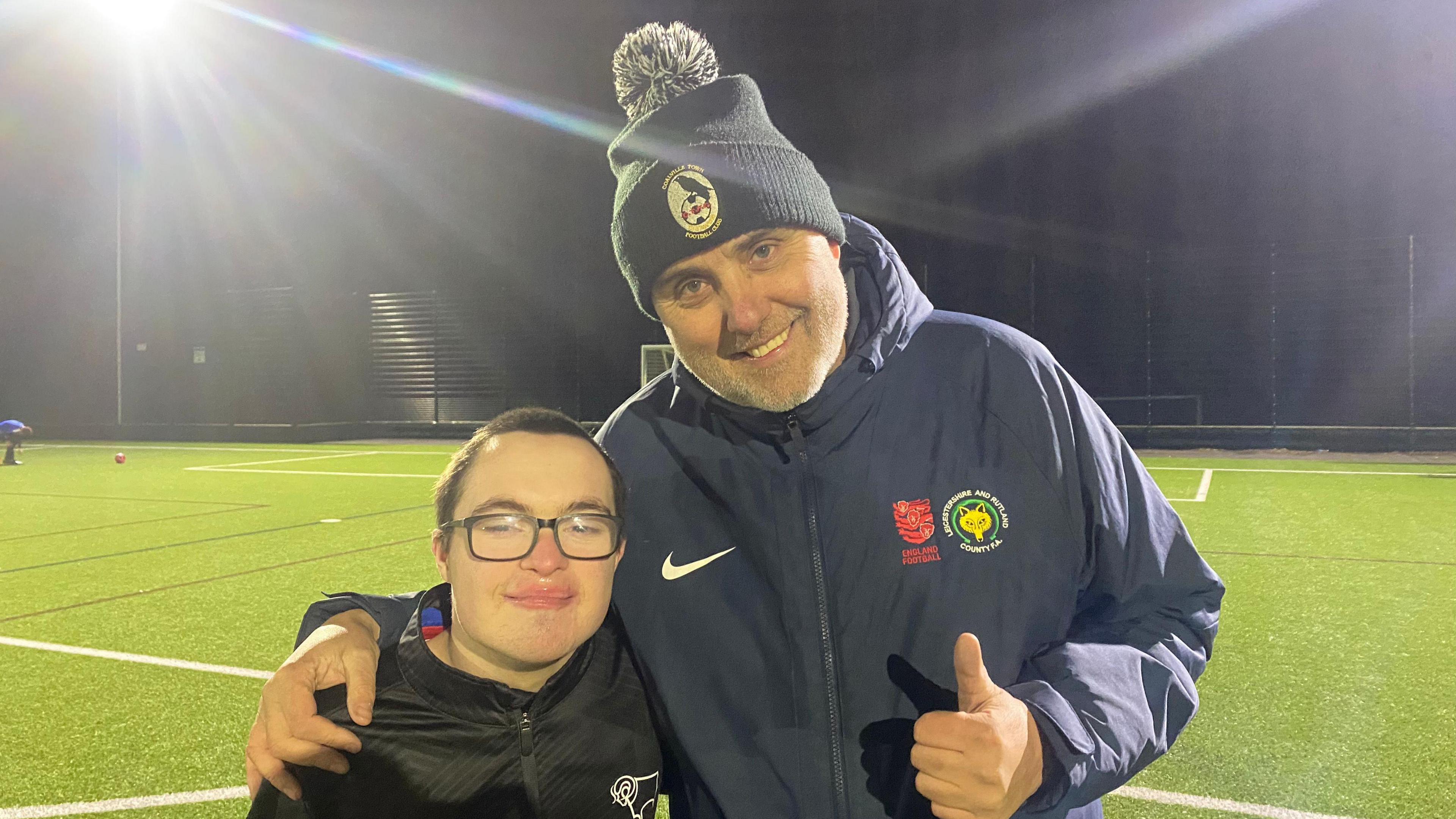 Mr Culpin and Riley dressed in warm clothes standing on a green 3G football pitch