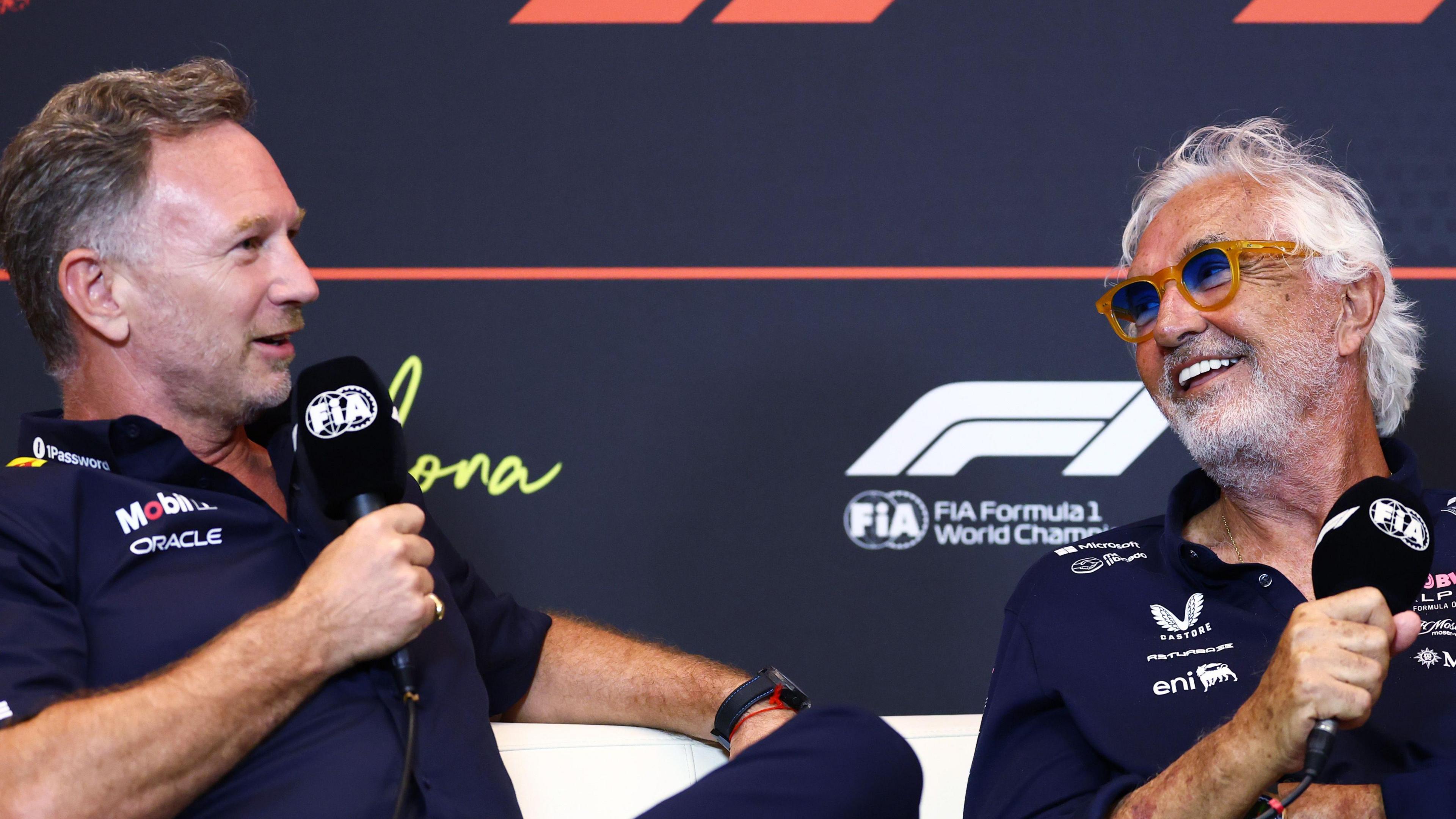 Christian Horner and Flavio Briatore speaking into FIA-branded microphones at a Formula 1 news conference