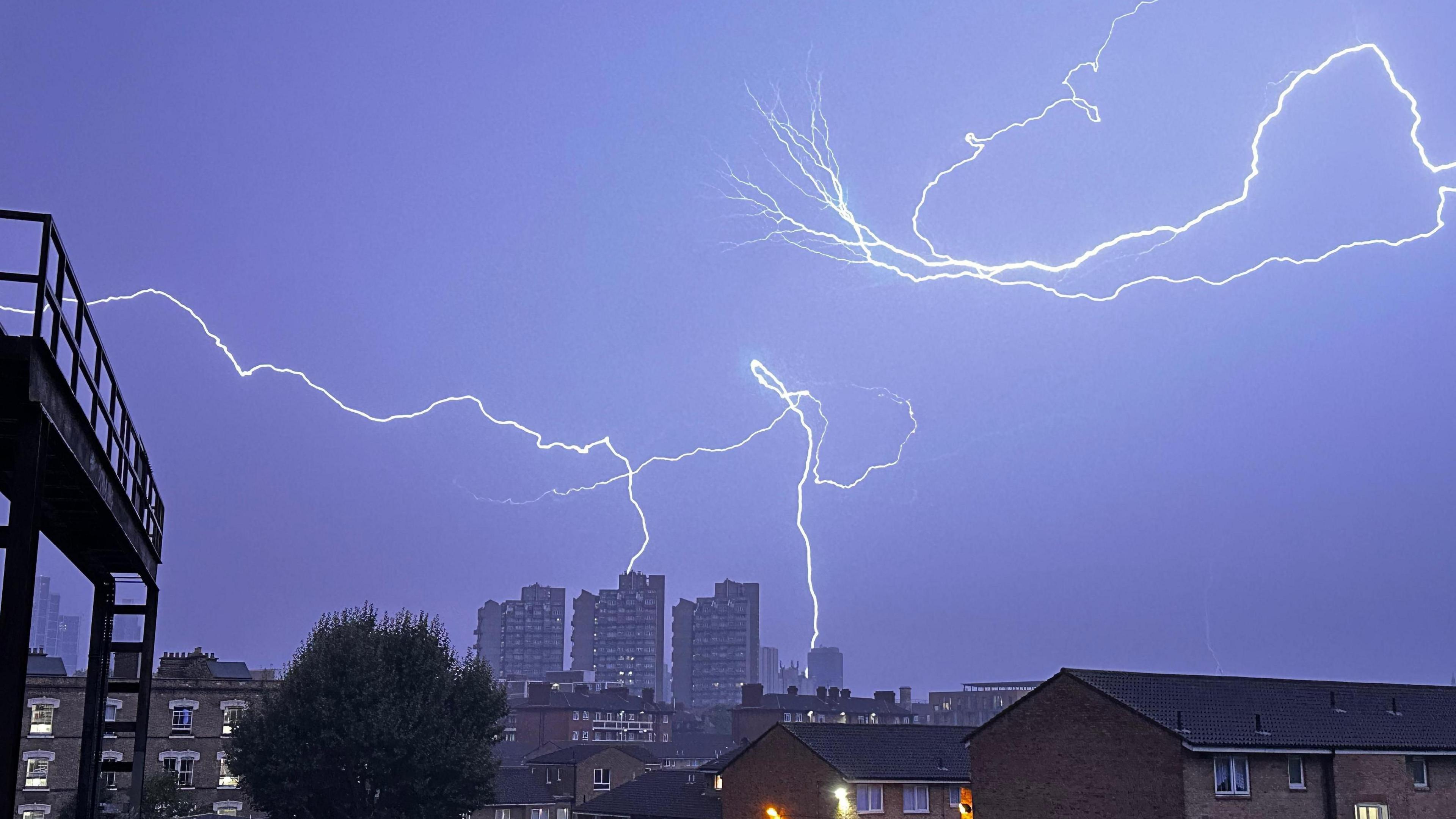 Forked lightning fills the darkened sky with some lightning hitting some high rise buildings in the distance