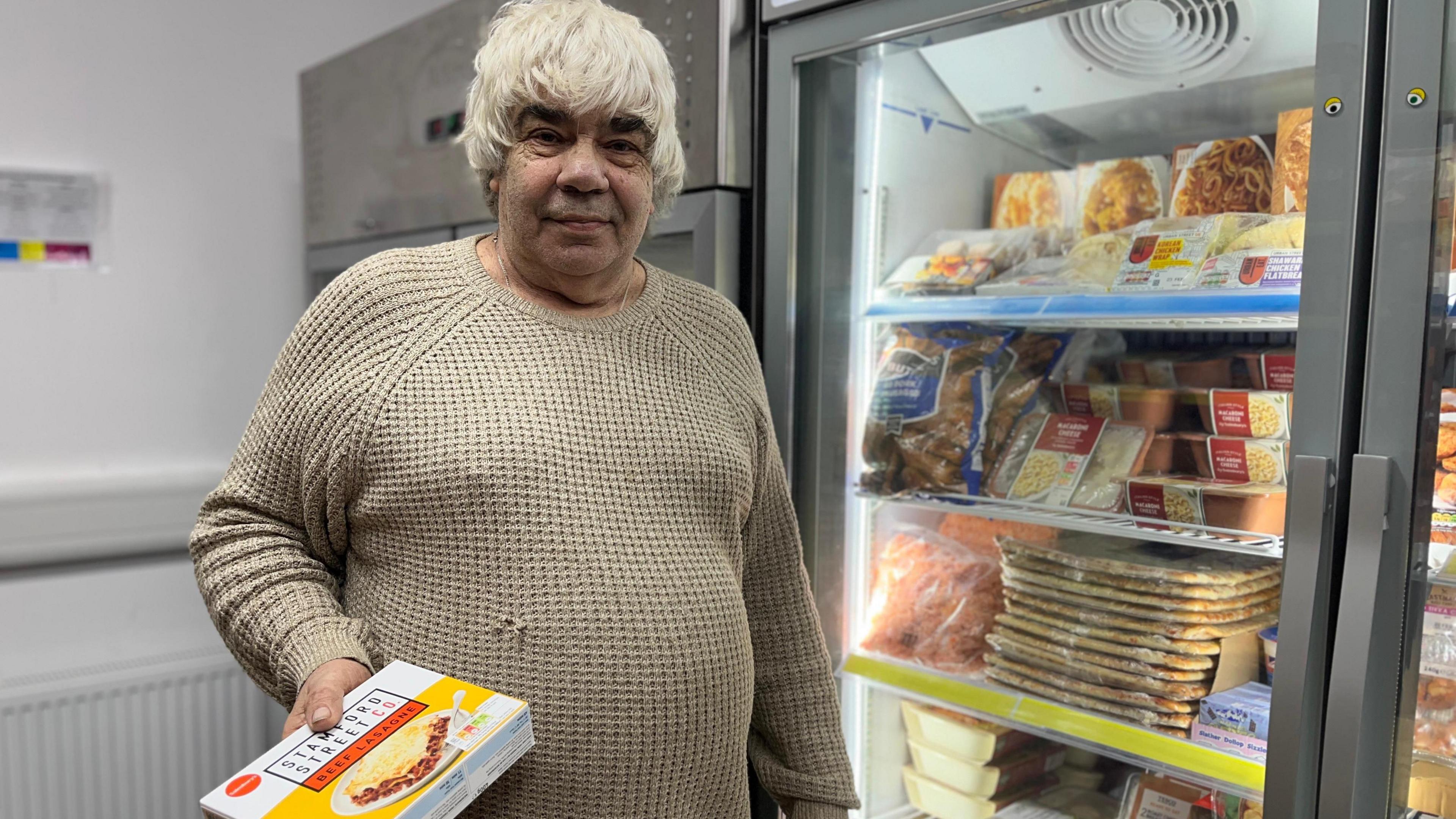 Melvyn Moyes stands by a freezer, holding a frozen lasagne 