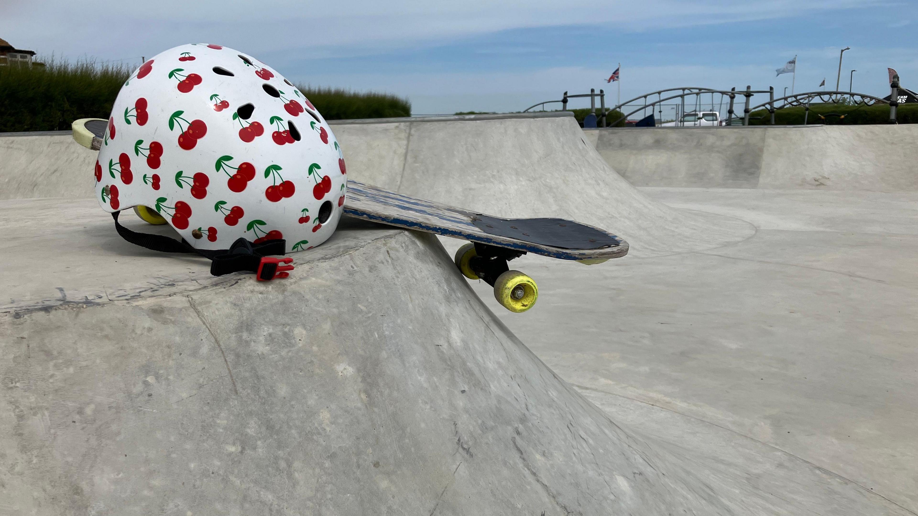 Skateboarding helmet with cherry design on it next to a skateboard lying on the new skatepark