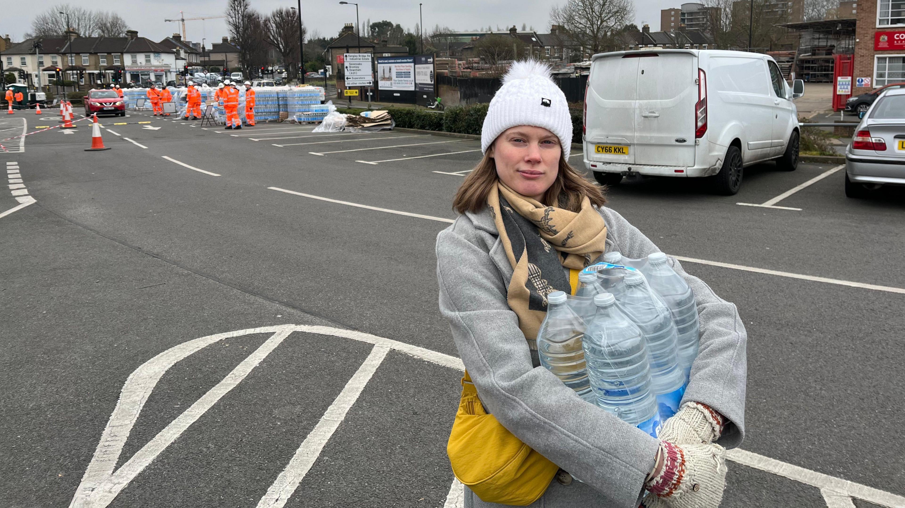 Charlotte stand holding six large bottles of water at the emergency water supply station 