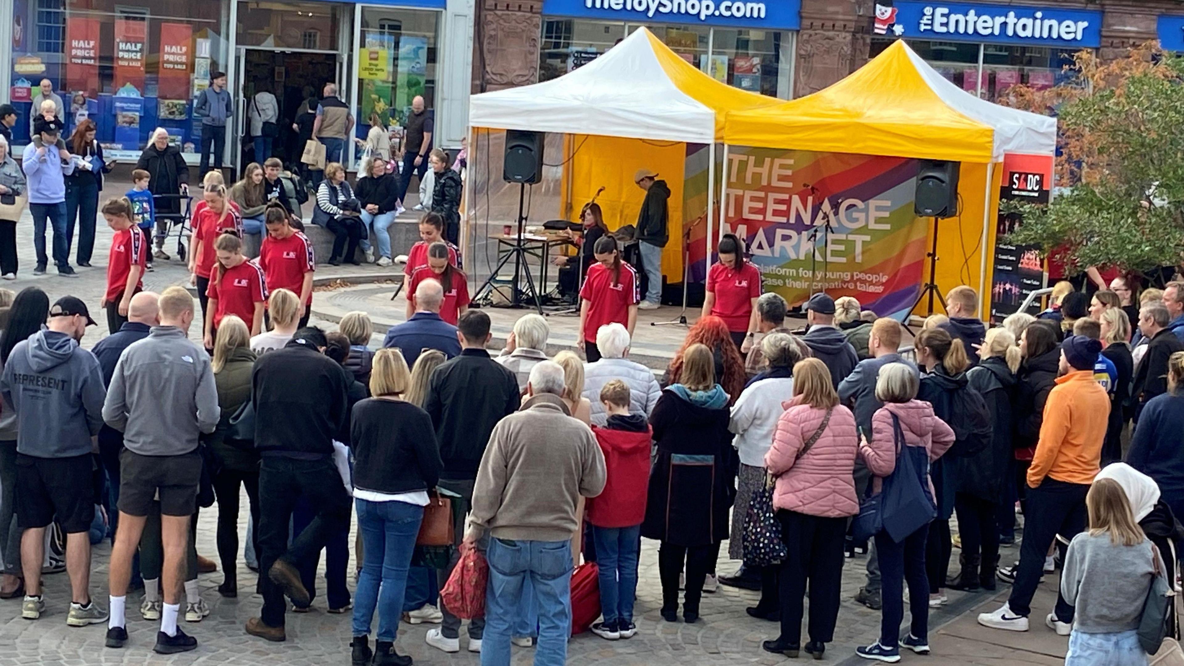 People watching a dancers in red t-shirts perform at the Teenage Market.