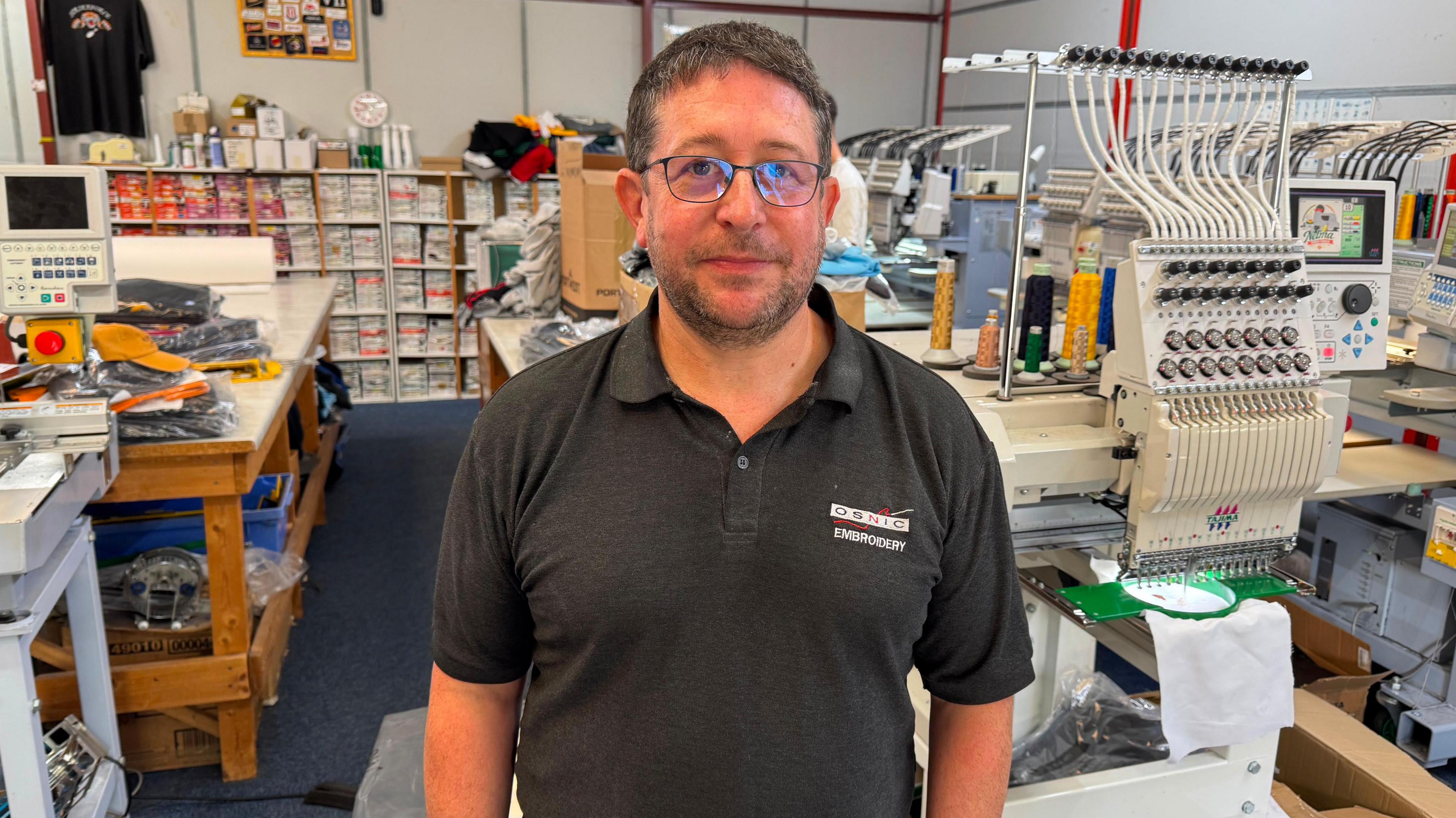 A man is standing in a black polo shirt with branding machinery behind him