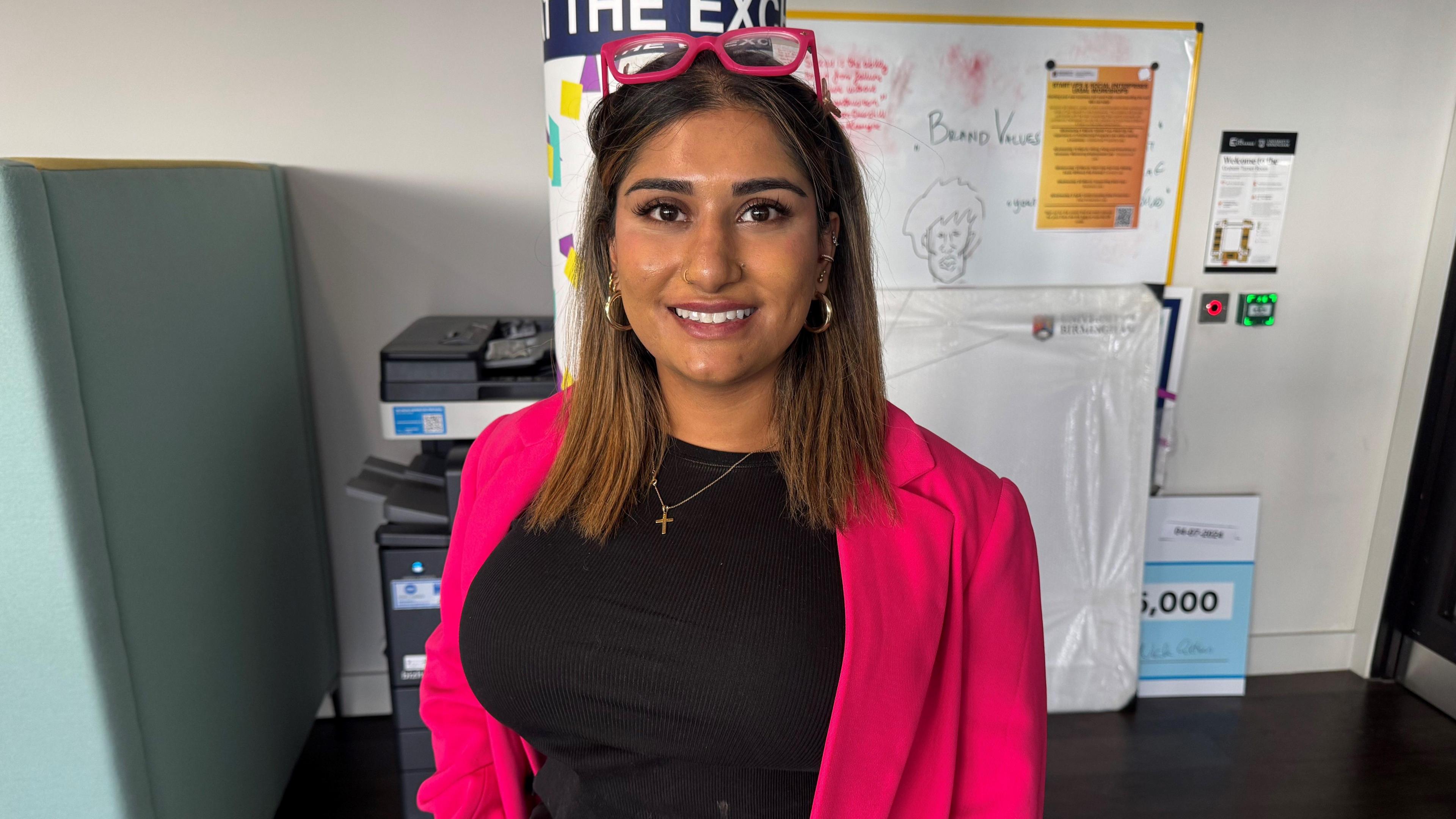 A woman wearing a pink blazer and black t-shirt looks into the camera.